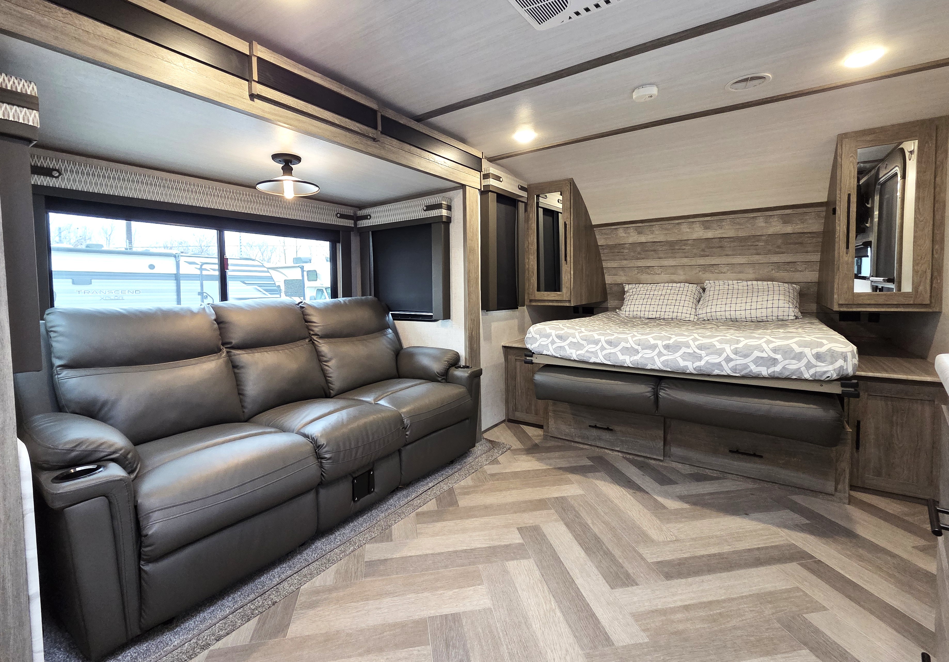 Cozy rv rental interior features a dark sofa, bed with storage, wood accents, and herringbone flooring.. Forest River Wildwood Heritage Glen HL 2021