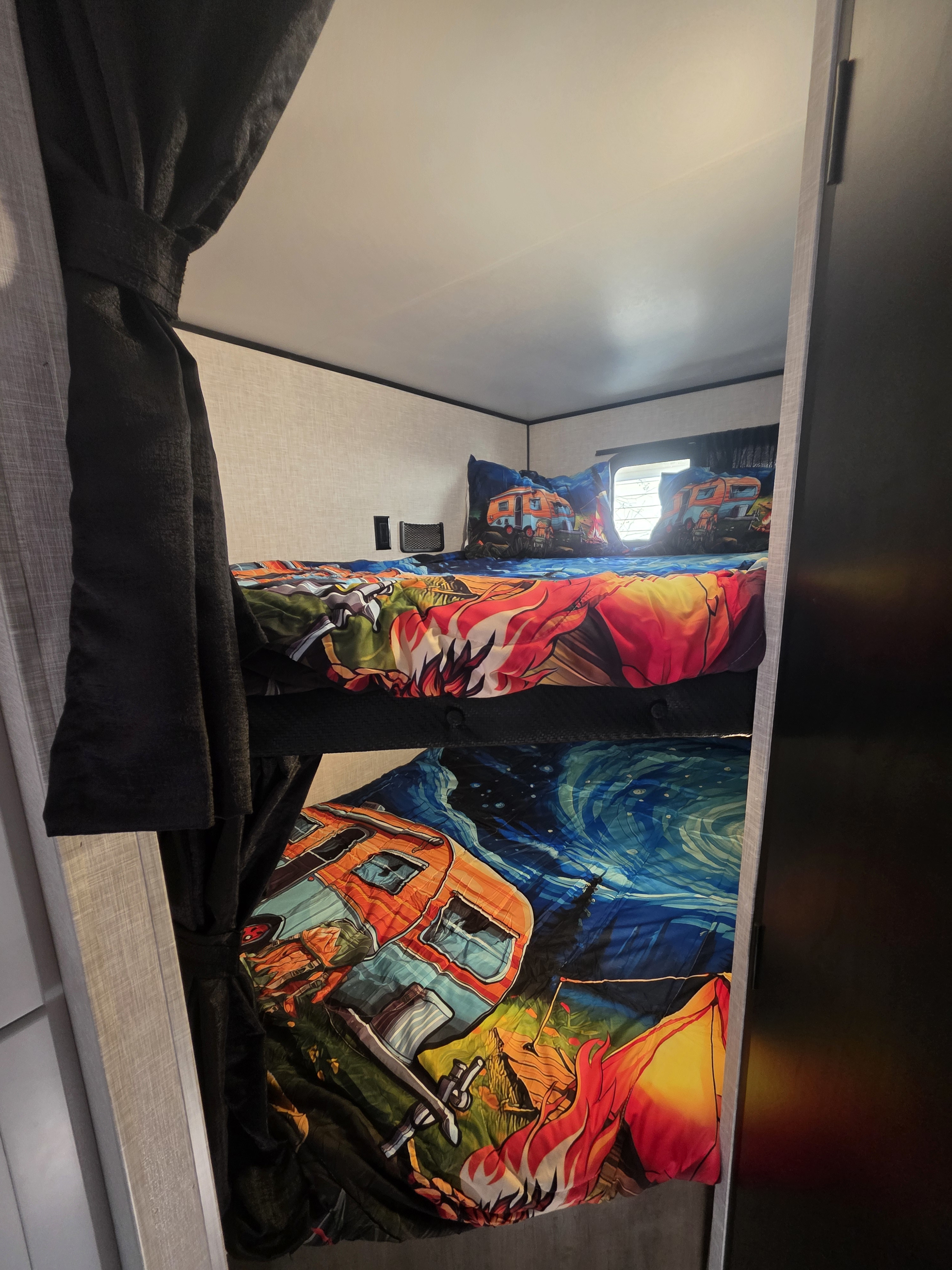 Bunk beds inside an rv rental, featuring vibrant camping-themed bedding with camper van and fire illustrations.. Highland Ridge RV Open Range 2025