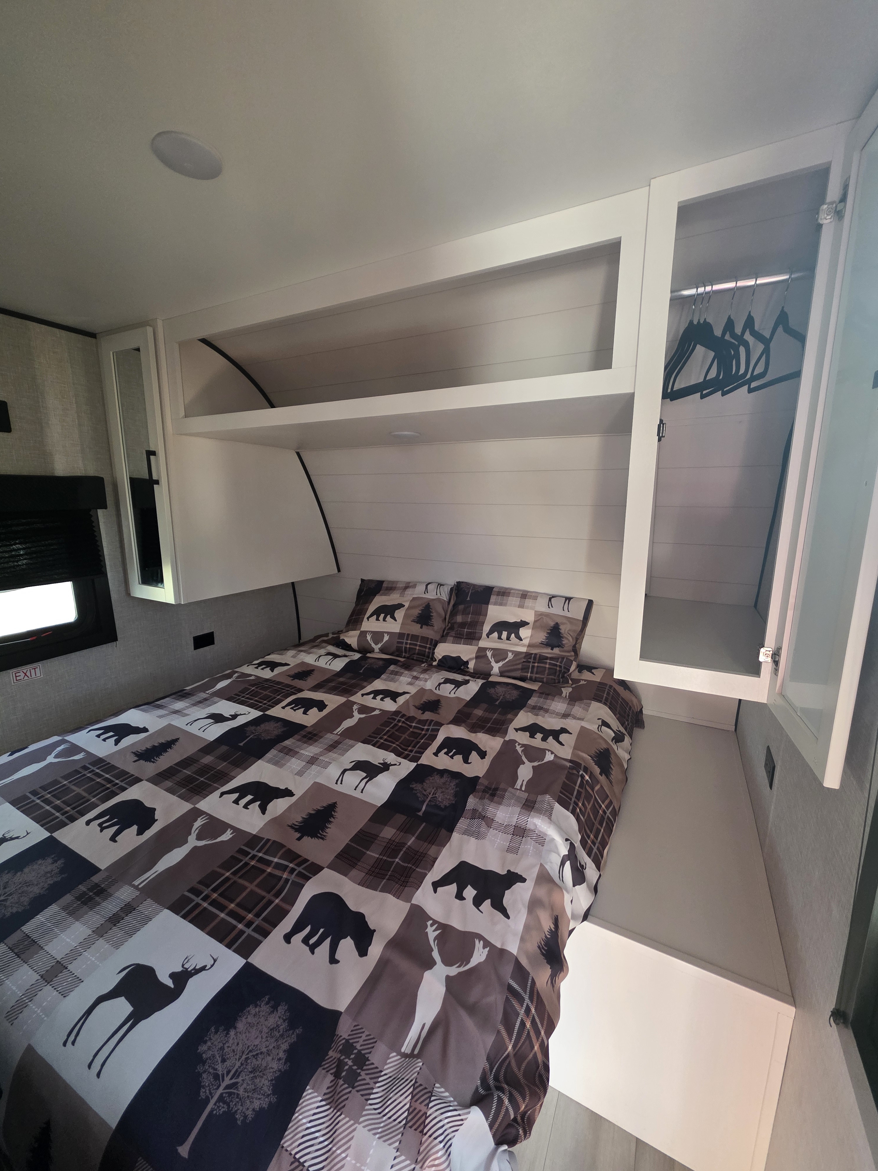 Cozy RV rental bedroom with wilderness-themed bedding, overhead storage, and a small closet.. Highland Ridge RV Open Range 2025