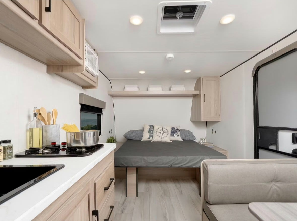 RV rental interior featuring a compact kitchenette, cozy bed, overhead storage, and a small dining nook.. Keystone RV Coleman 2025