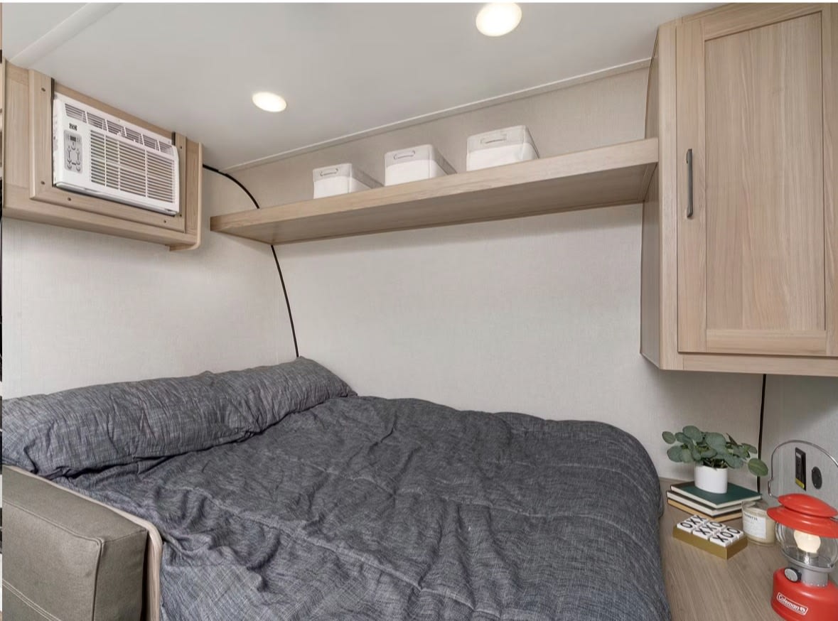 Cozy RV rental bedroom with gray bed, AC unit, overhead shelf for storage, and wood cabinet.. Keystone RV Coleman 2025