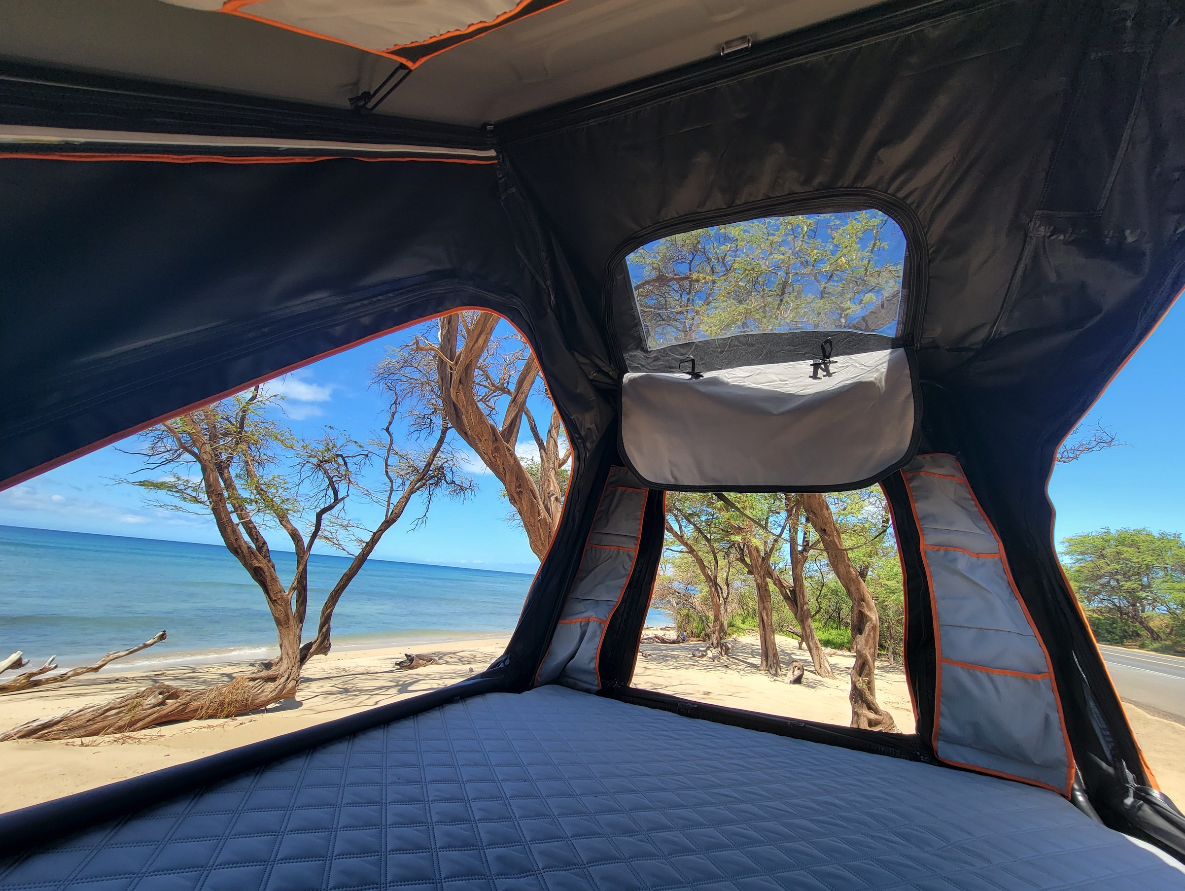 Inside a comfortable rooftop tent setup, offering a picturesque ocean view and sandy beach. Ideal for your RV rental getaway.. Toyota 4 Runner 2025
