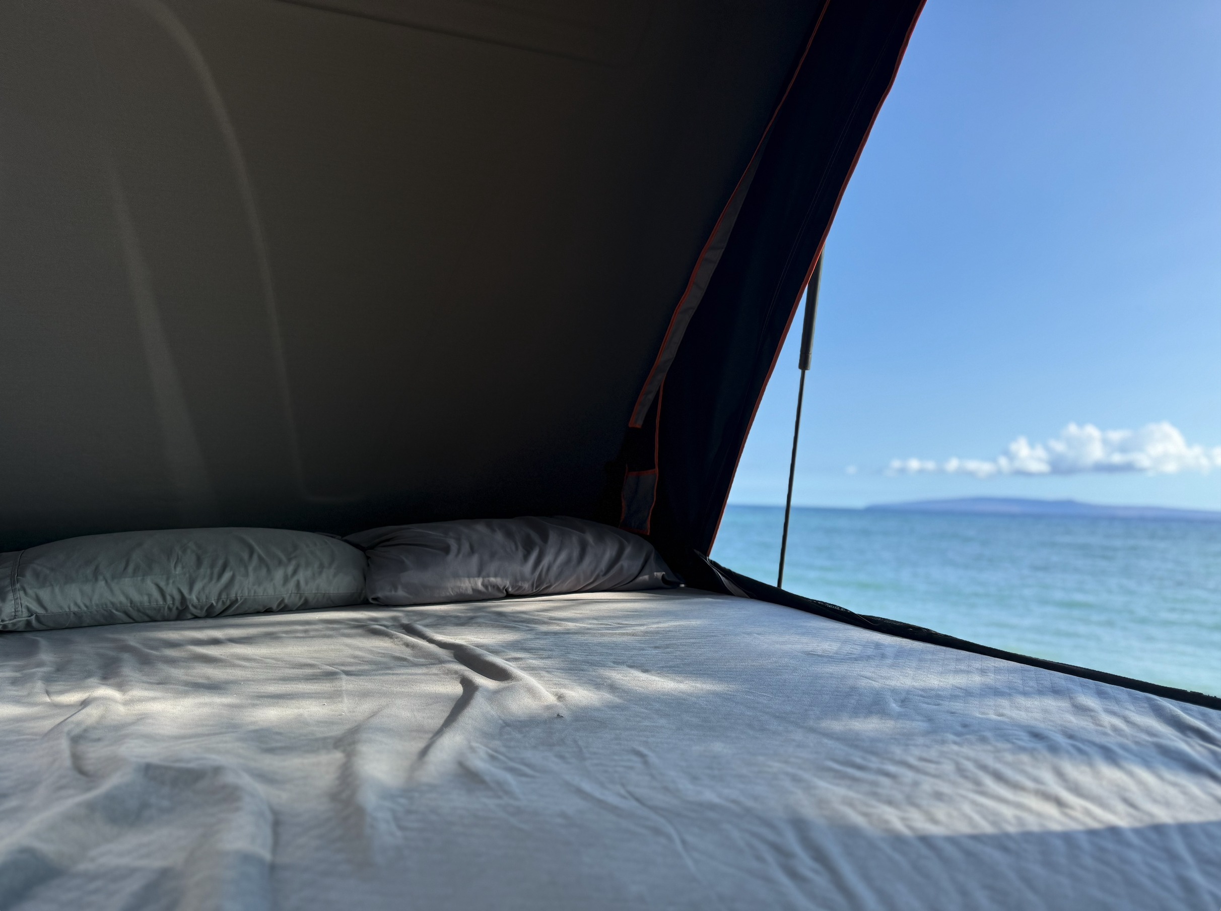 RV rental with a view! Inside a pop-top RV, a made bed offers stunning ocean views, perfect for beachside camping.. Toyota 4 Runner 2025