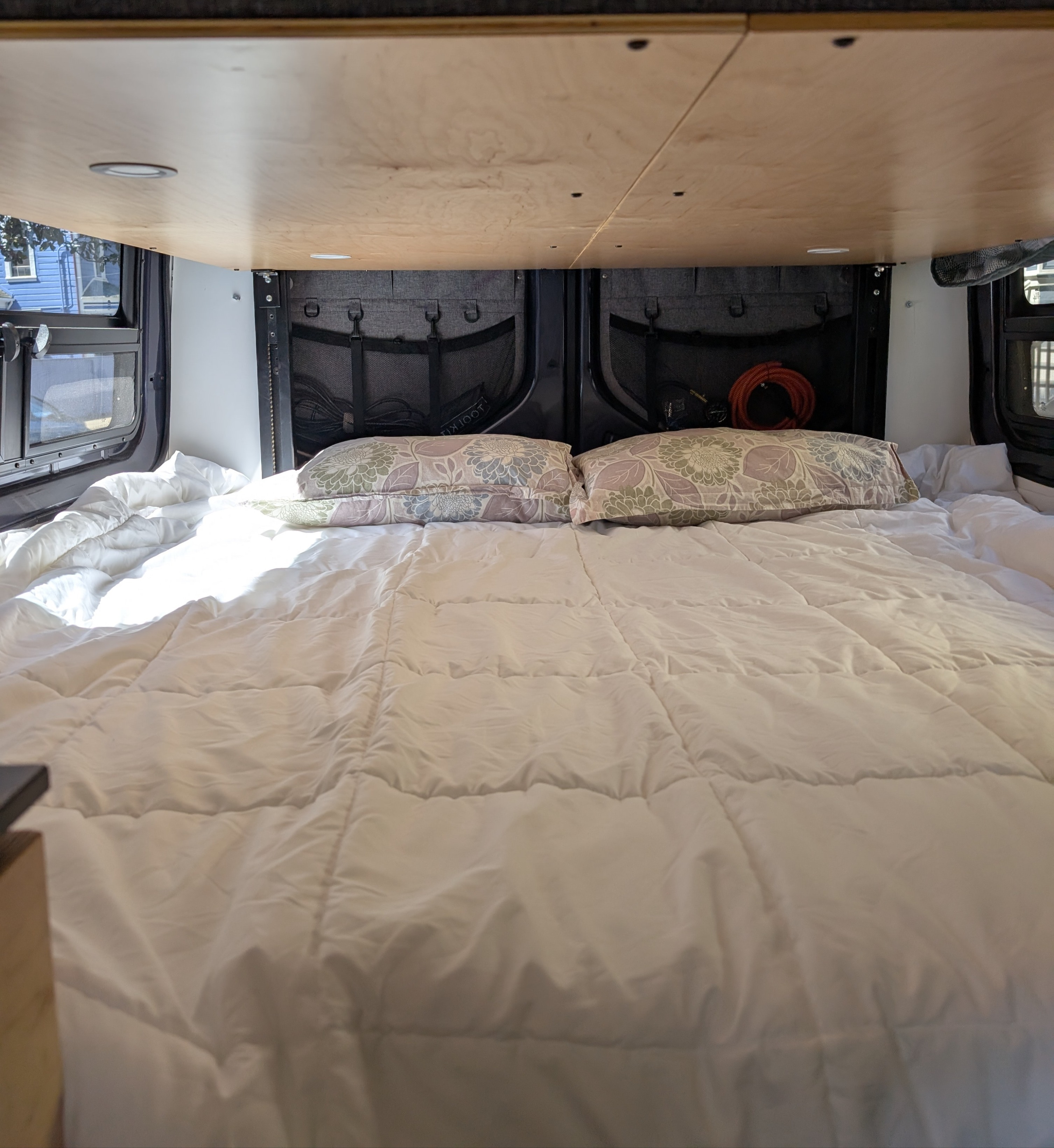 Comfortable RV rental bed with white comforter, patterned pillows, and overhead lighting in a camper van.. Mercedes 4WD Sprinter 2500 (170 wheelbase) 2021