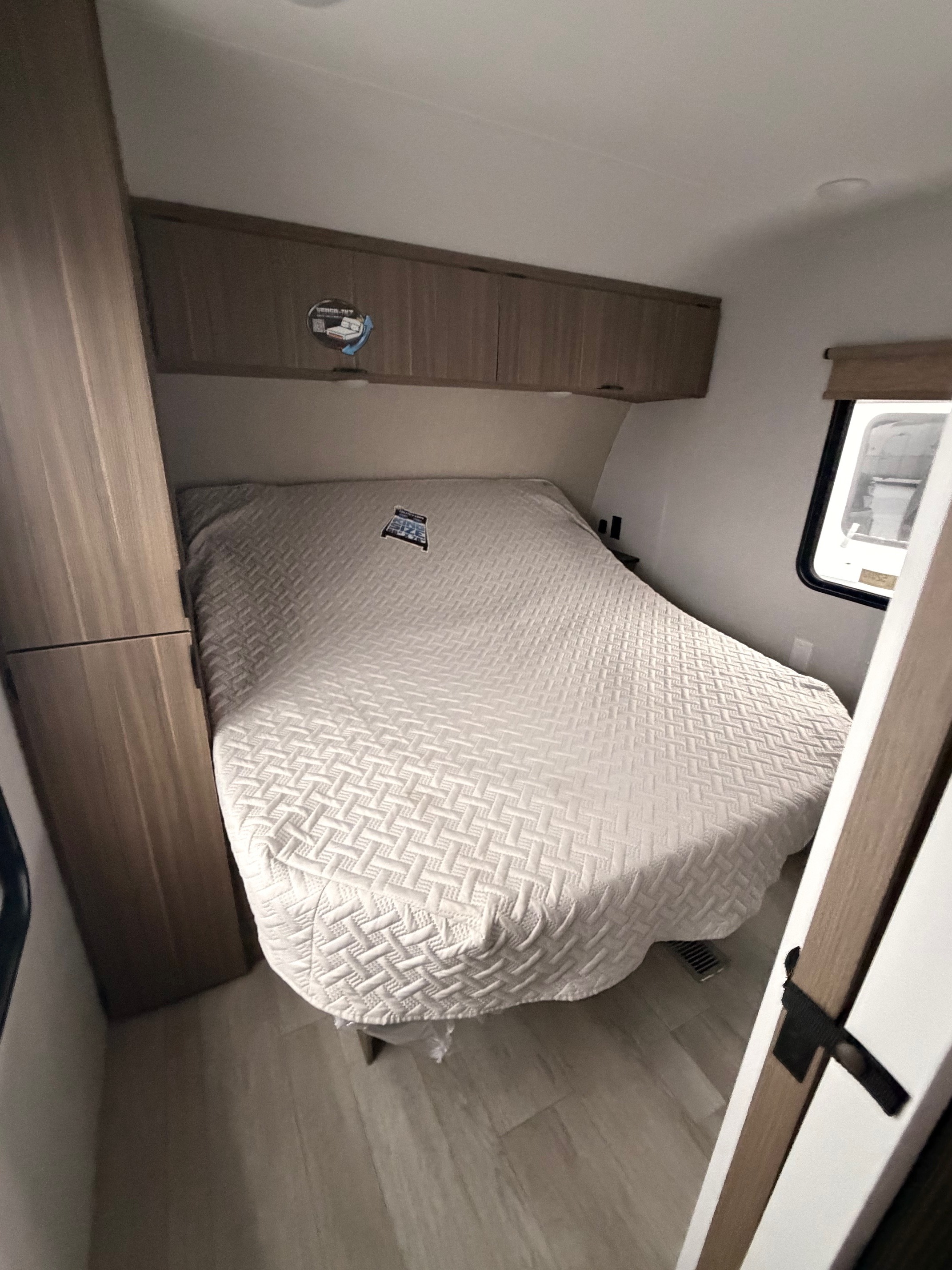 Cozy RV rental bedroom with a white quilted bed, wood cabinets, and window, featuring a versatile Versa-Tilt bed design.. Forest River Wildwood 2025