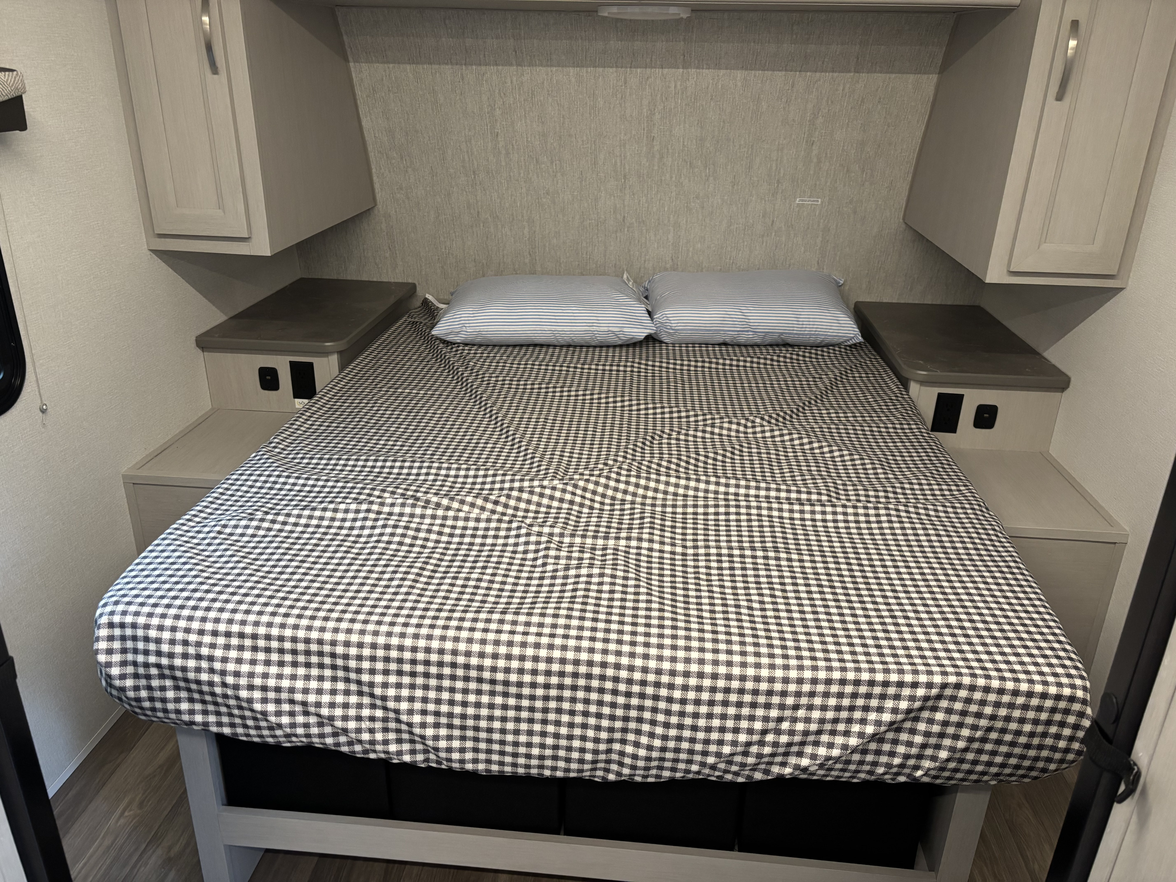 Cozy RV rental bedroom featuring a bed with a black and white gingham duvet, striped pillows, and nightstands with outlets.. Cruiser RV Shadow Cruiser 2025