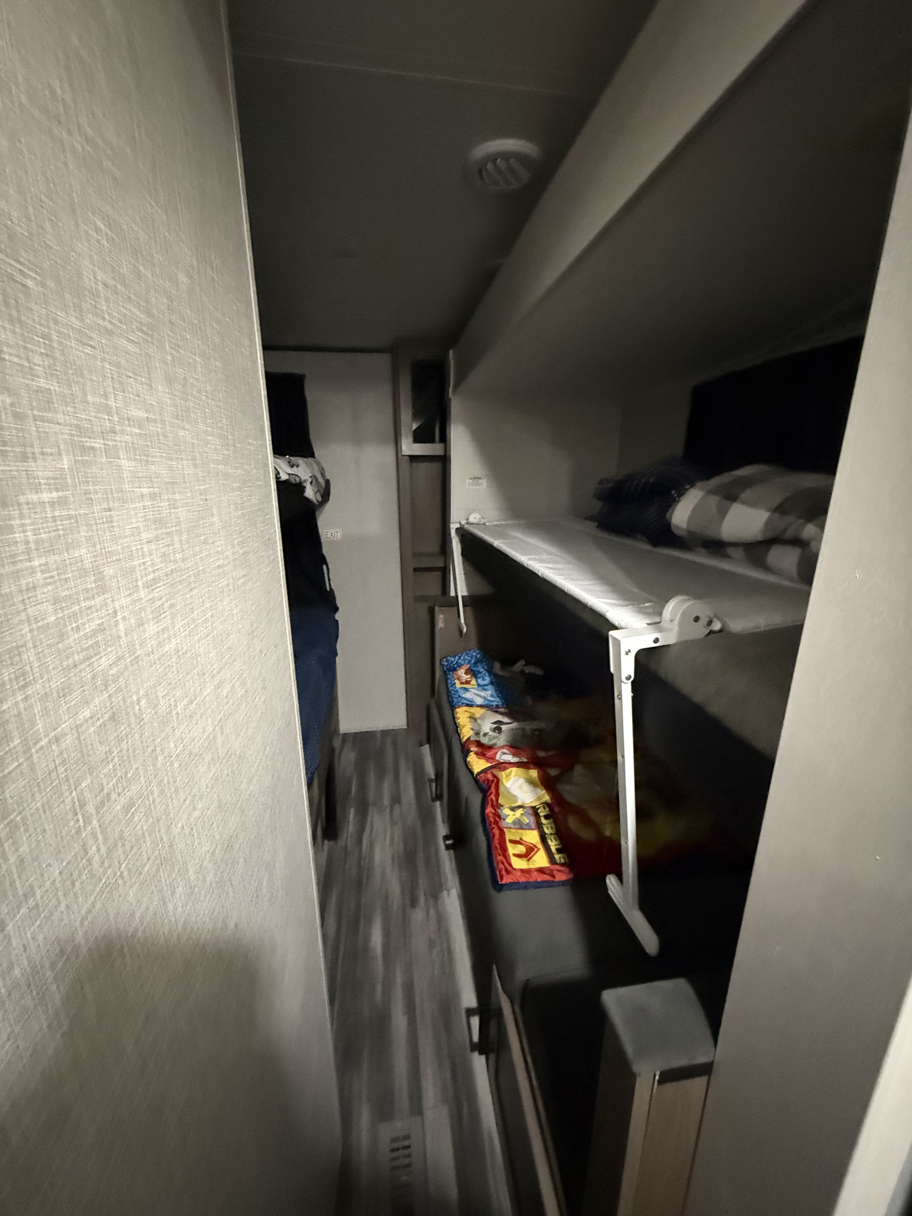 Narrow hallway of an RV rental leading to bunk beds. Lower bunk has colorful blankets, upper bunk has plaid bedding, ceiling vent visible.. Jayco Jay Flight SLX 2025