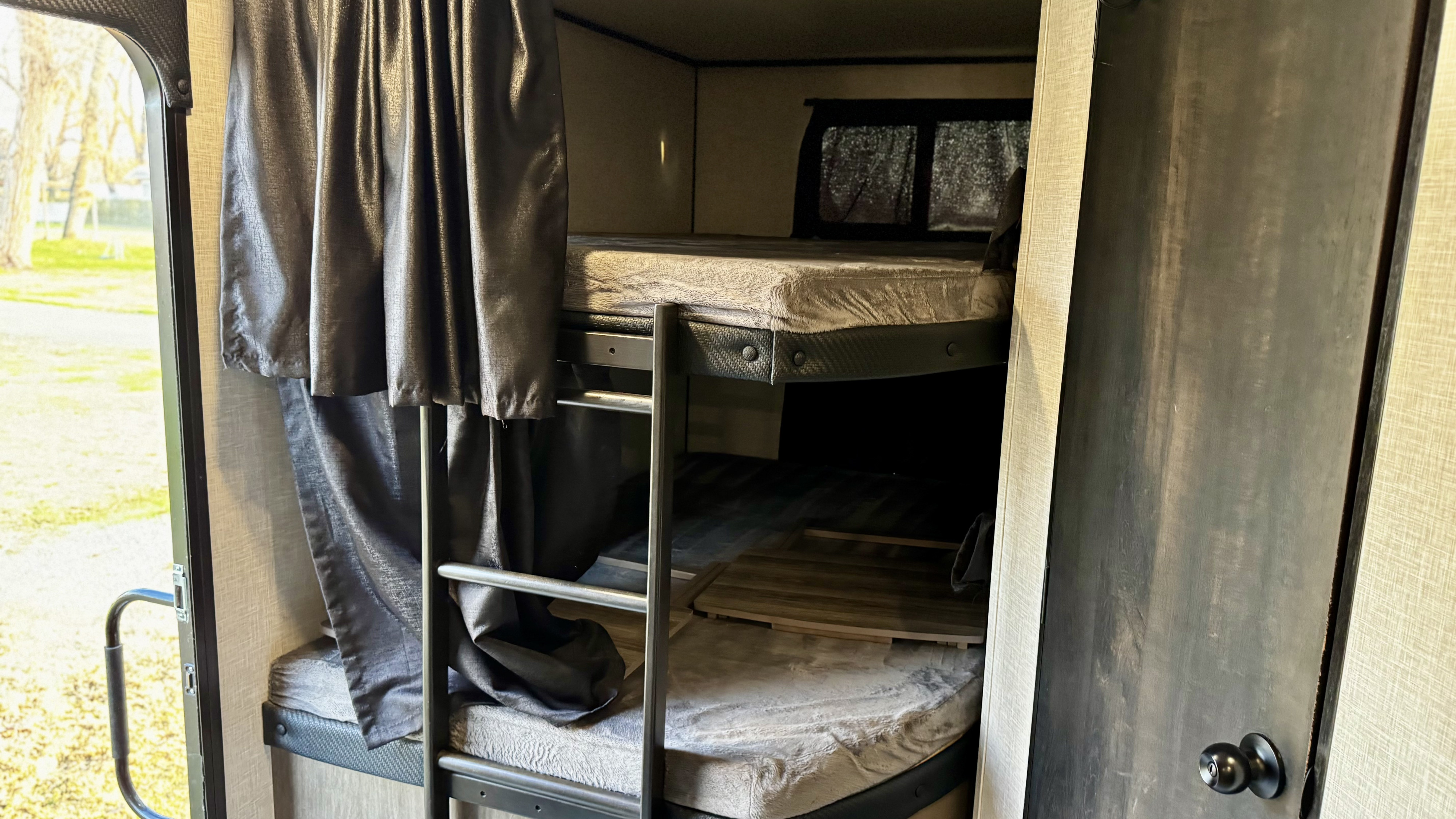 Inside an RV rental, a cozy bunk bed area with dark curtains, a ladder, and a window view to the outside.. Jayco Jay Flight Baja Edition 2024