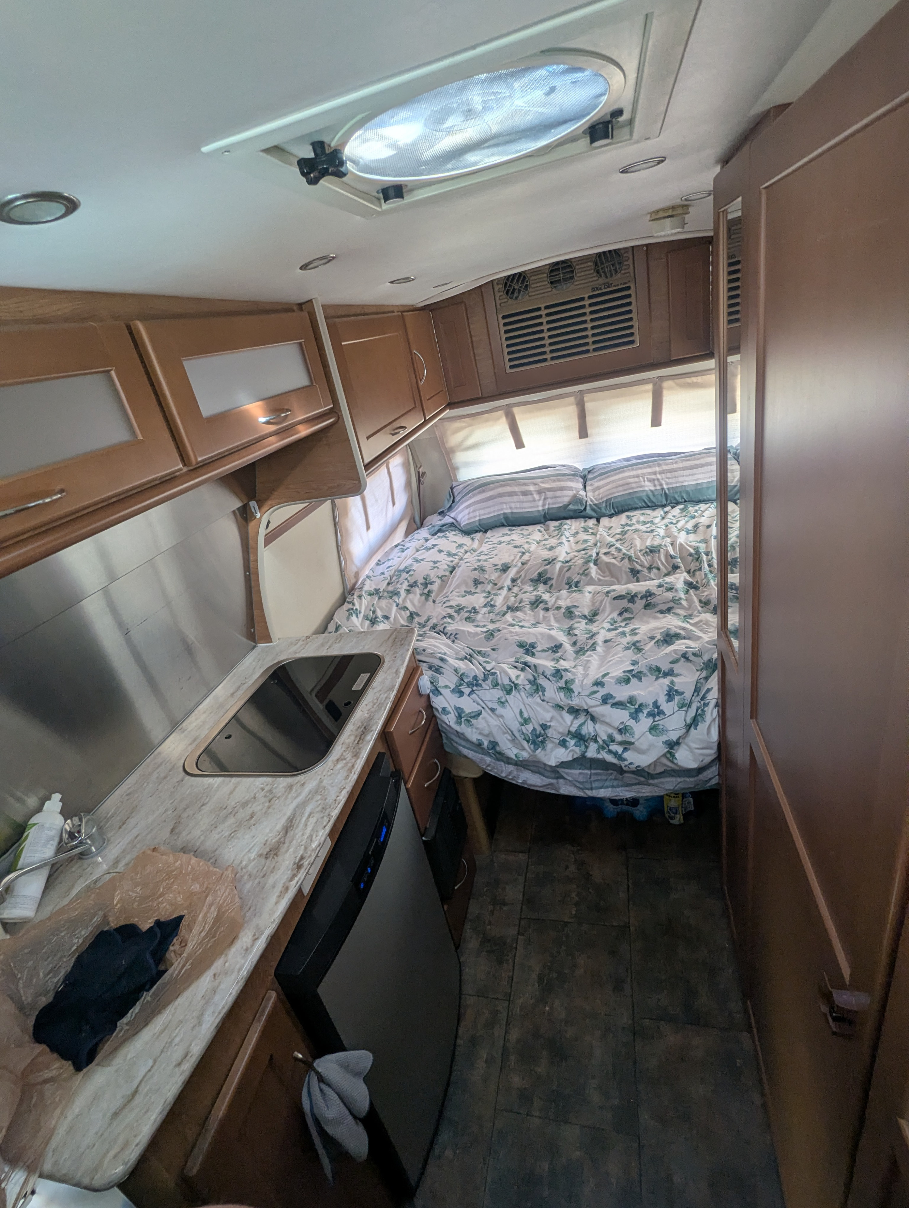Inside an RV rental: full view of the bedroom area with a floral duvet, kitchenette with a sink, and mini-fridge.. Pleasure-Way Excel TS 2012