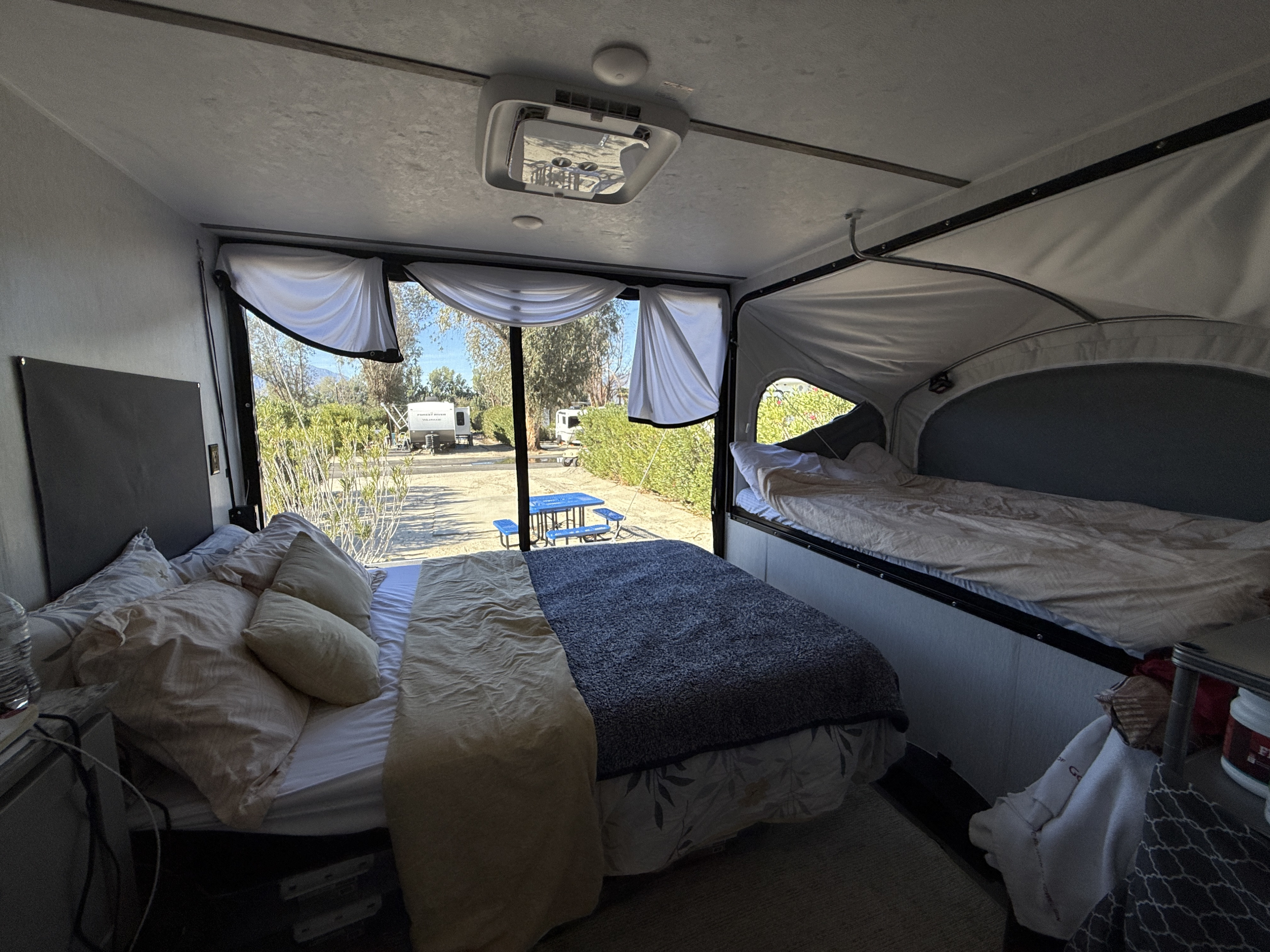 Cozy RV rental interior showing a main bed and an elevated pop-out bed, with a scenic campsite view outside.. Sun Lite 14 THX 2026