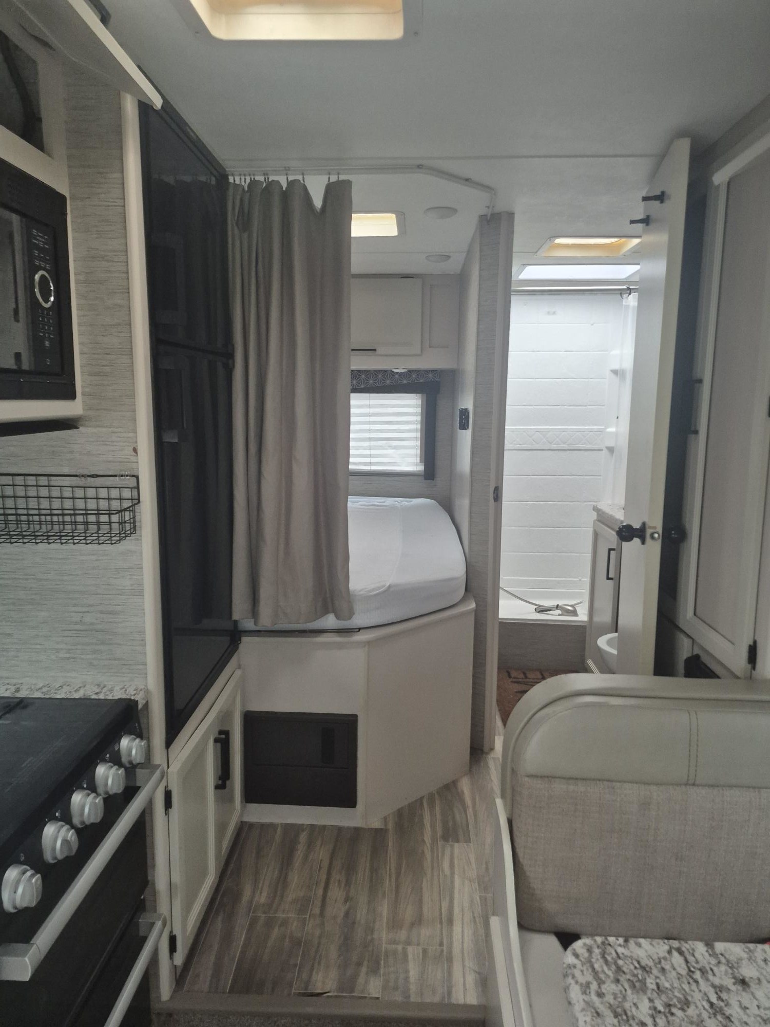 Interior of an rv rental: kitchen appliances & fridge on left, bed with privacy curtain, bathroom & seating area on right.. THOR MOTORCOACH 22HD 2022
