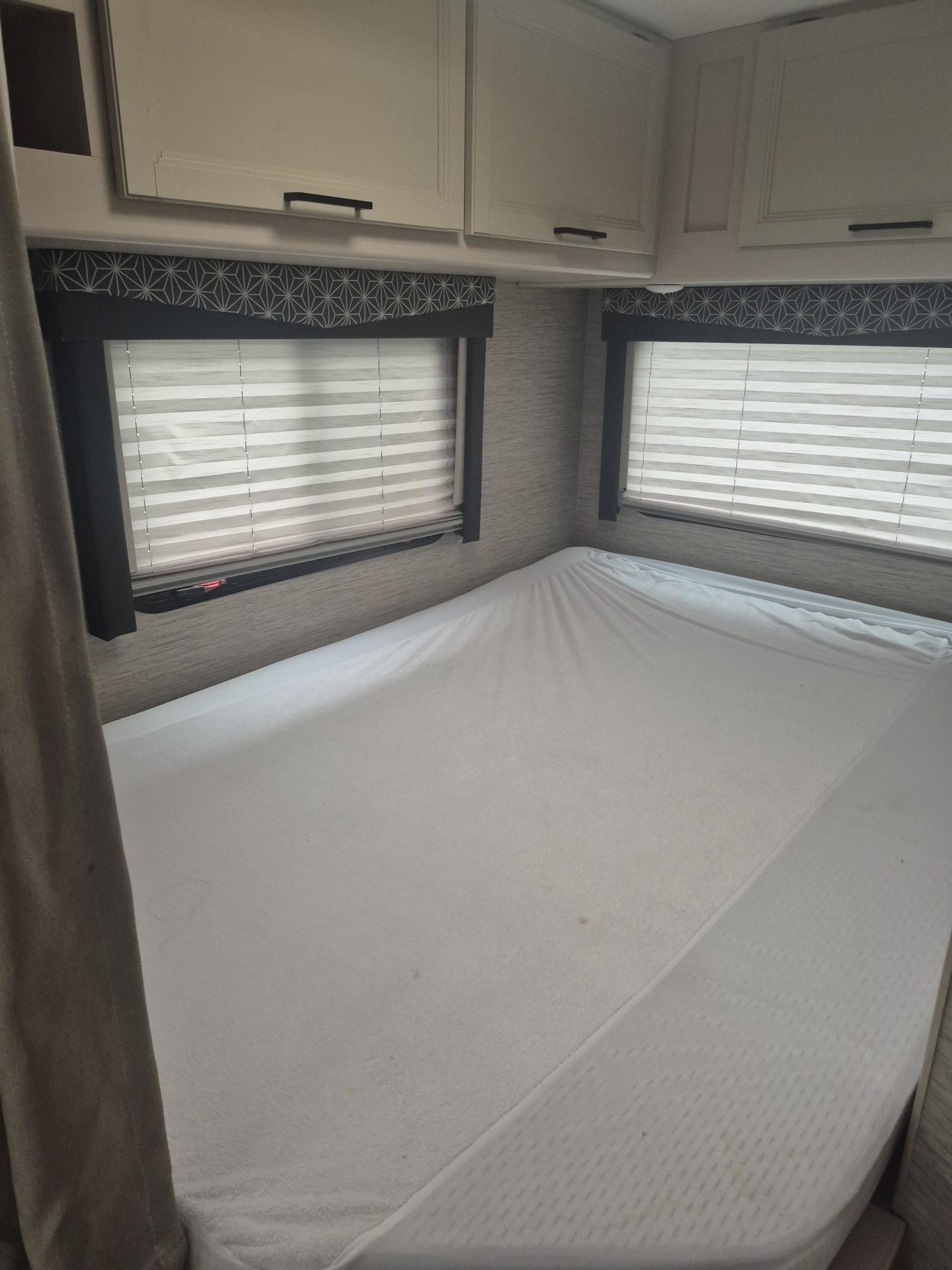 Cozy RV rental bedroom with a large bed, overhead storage cabinets, and window blinds with stylish patterned valances.. THOR MOTORCOACH 22HD 2022