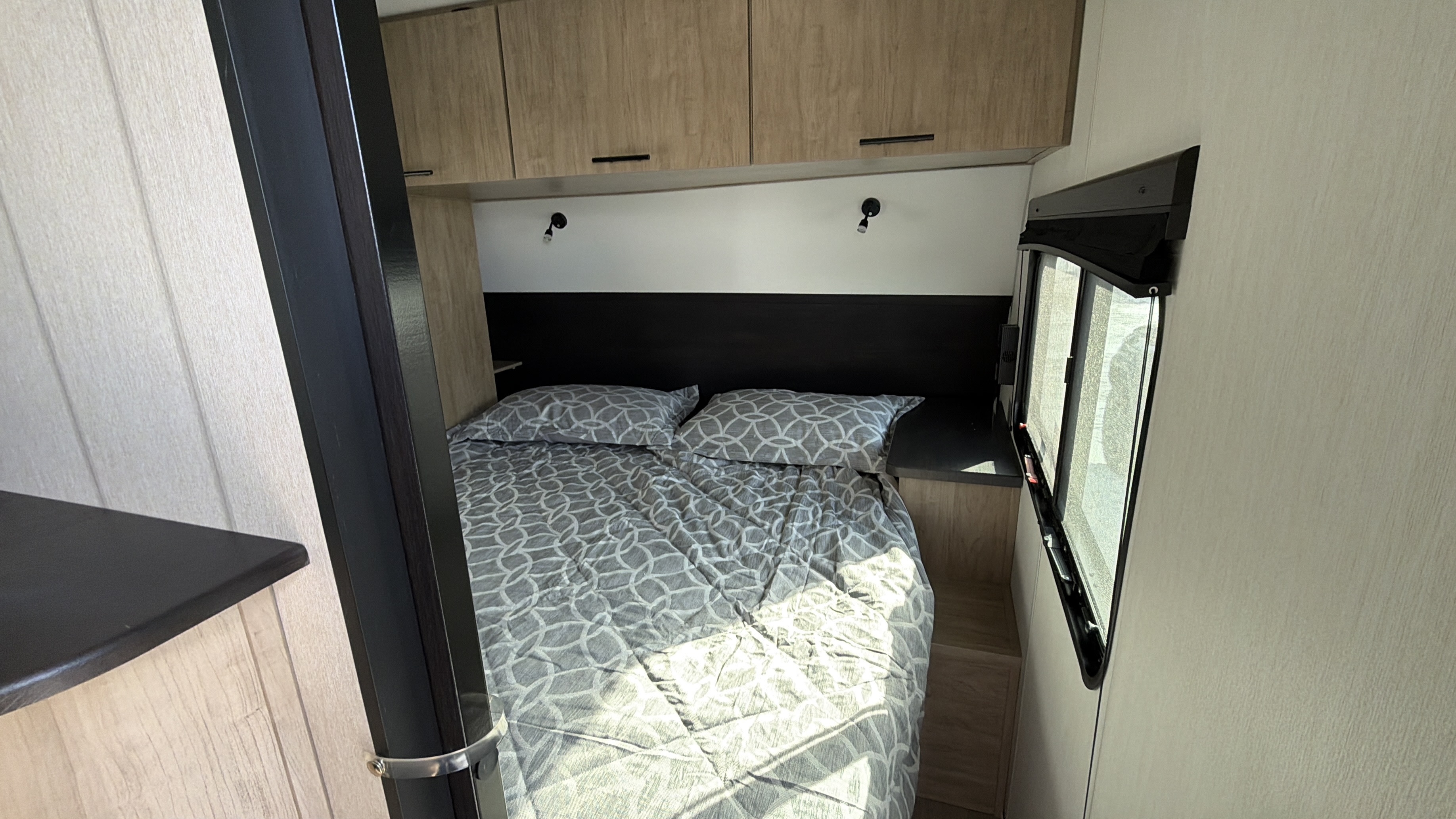 Bright RV rental bedroom showing a comfy bed with gray patterned bedding, overhead cabinets, and a side window for light.. Forest River Cherokee Grey Wolf Black Label 2026