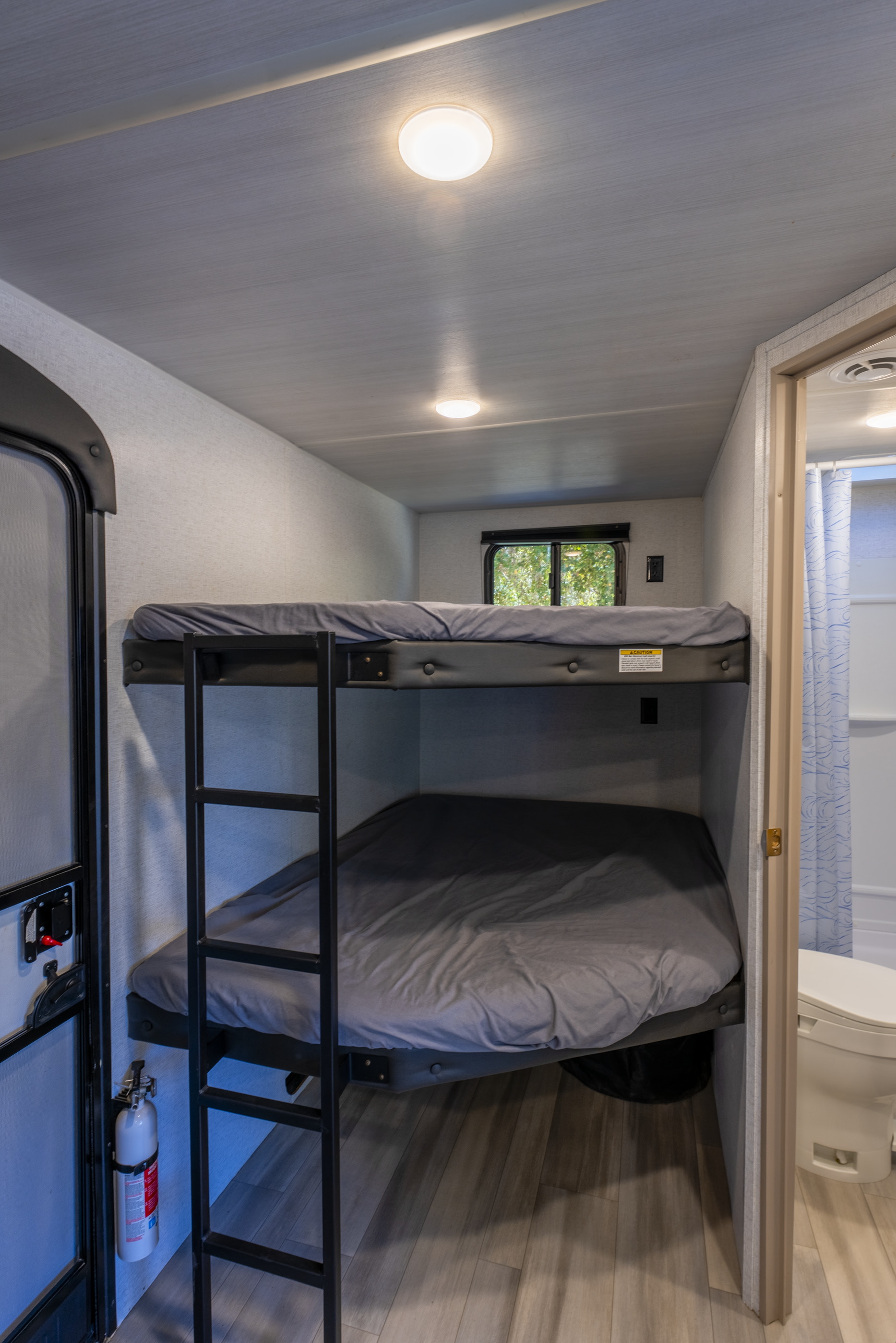 This RV rental offers a cozy bunk bed area with a ladder and window. A fire extinguisher is by the door, and a bathroom is adjacent.. Keystone Springdale 2024