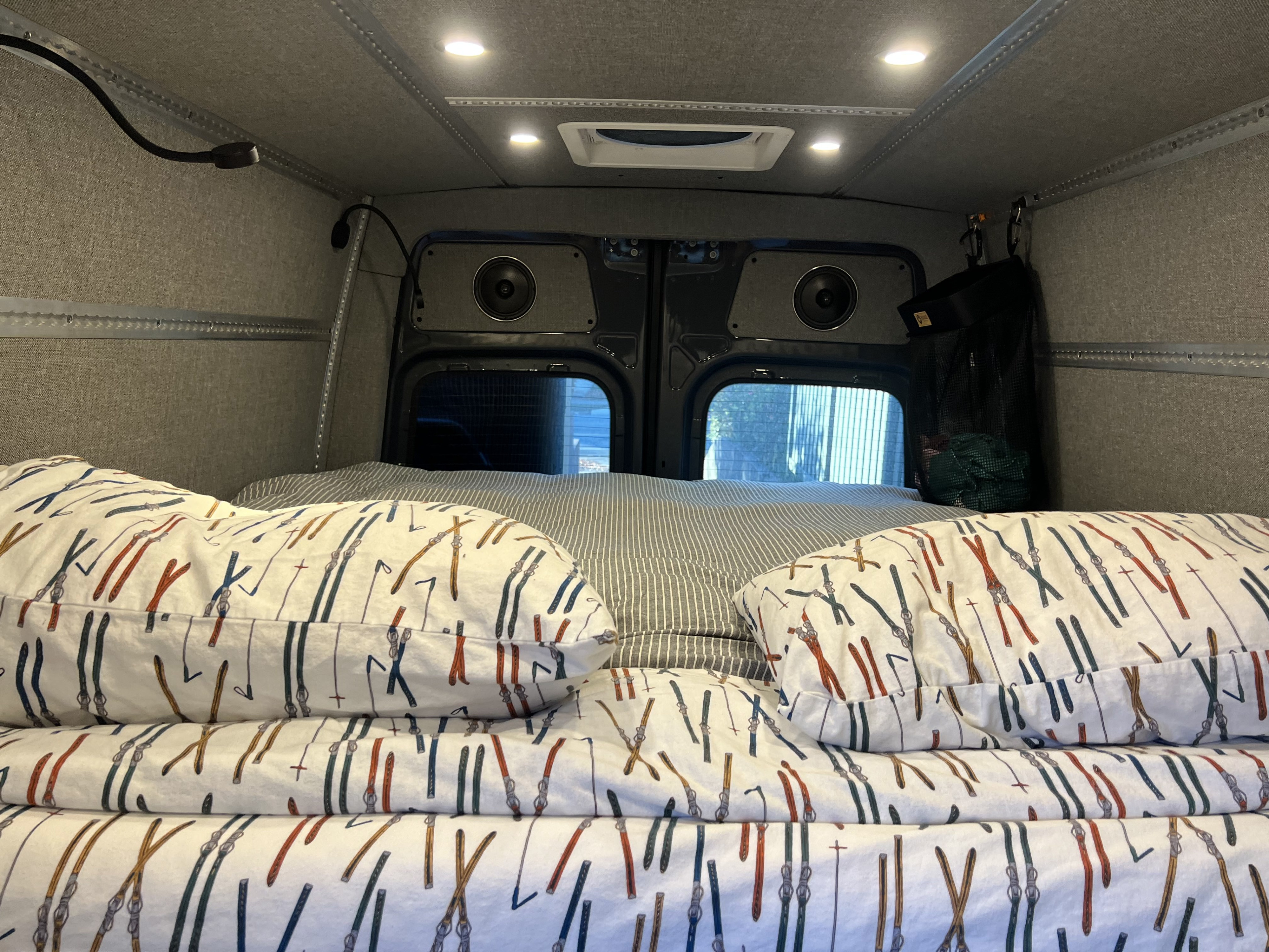 Cozy RV rental bed with ski-patterned bedding, built-in speakers, and ambient lighting, perfect for van life adventures.. Mercedes Sprinter 2022