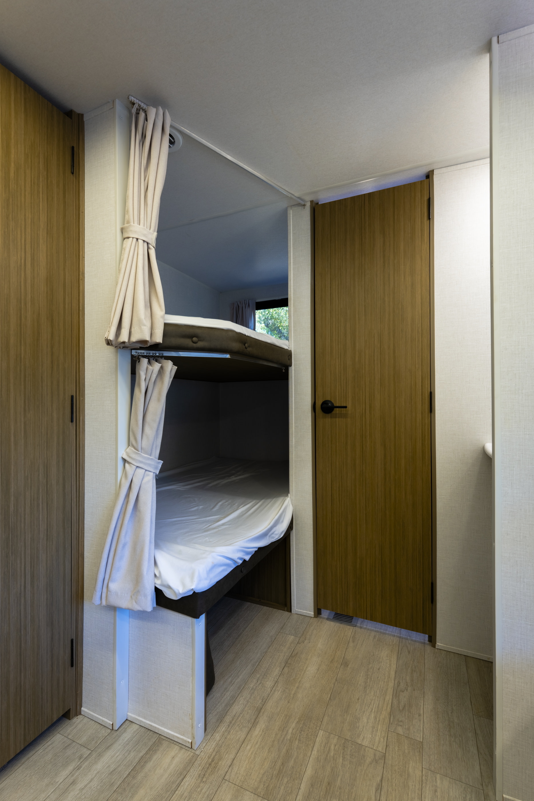 Cozy bunk beds in an RV rental, featuring privacy curtains and modern wood finishes for a comfortable travel stay.. Wildwood 28DBUD 2025