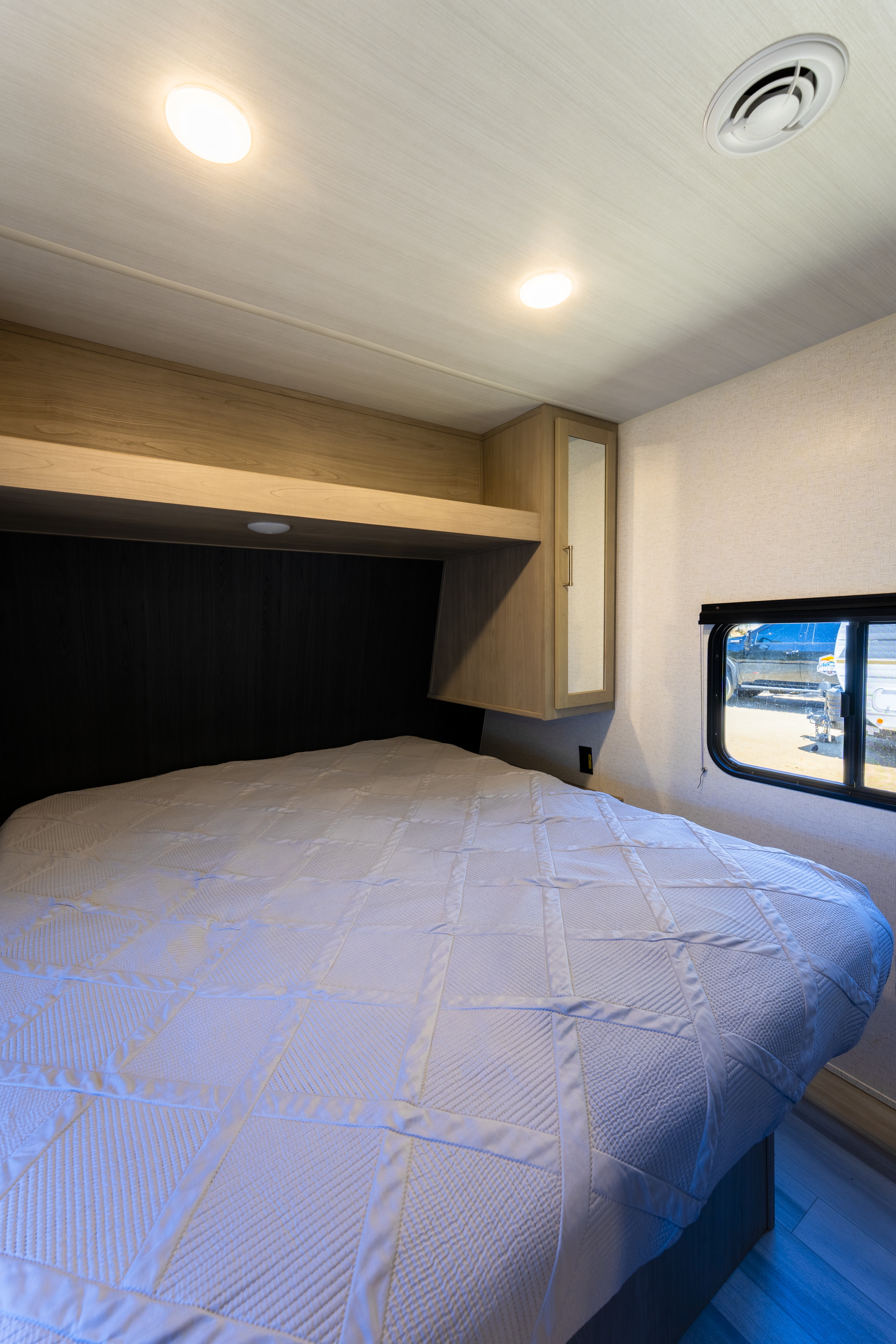 Cozy RV rental bedroom featuring a comfortable bed, overhead storage, lights, and a window for scenic views on your journey.. Wildwood 28DBUD 2025