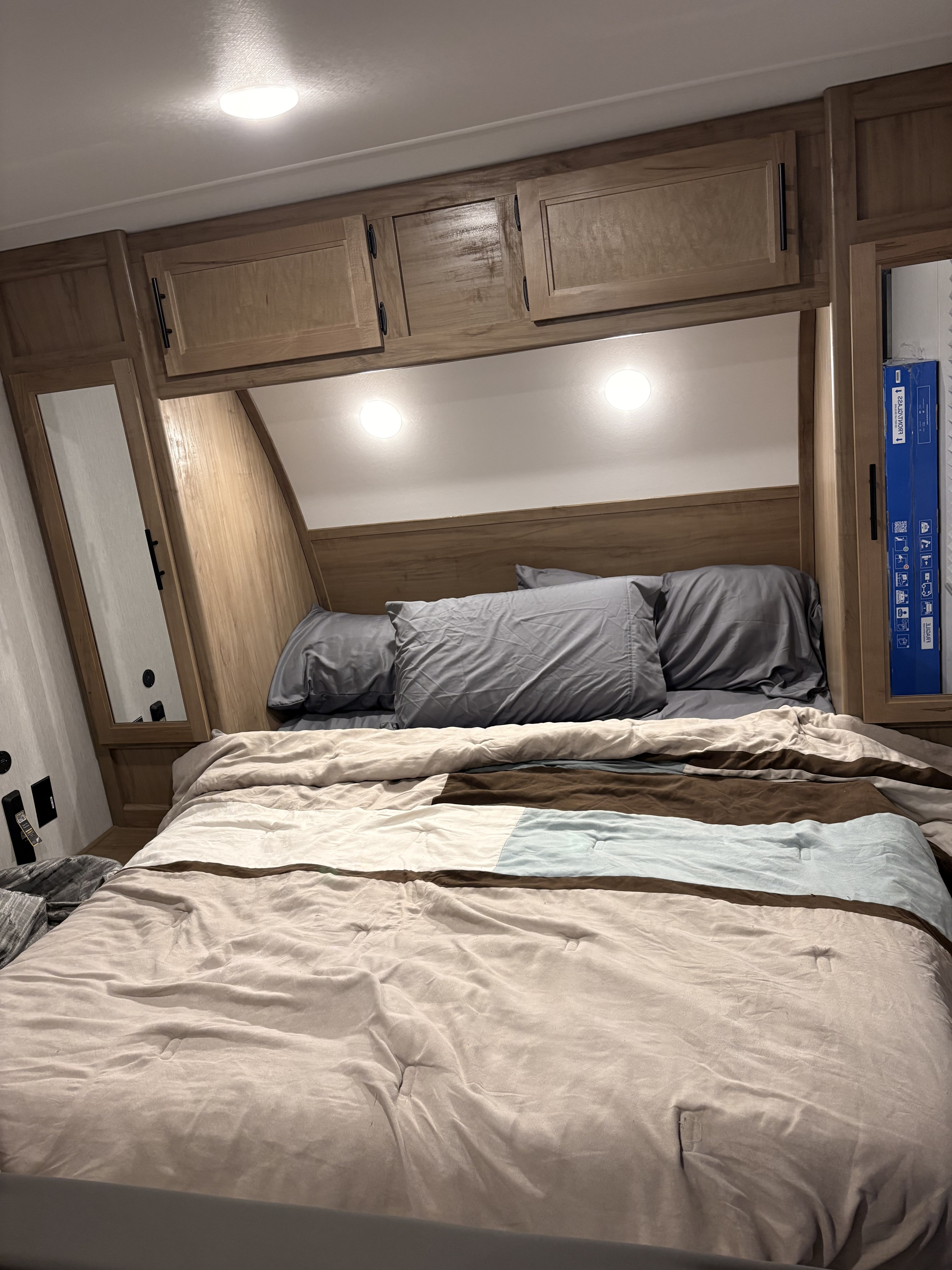 Cozy RV rental bedroom with a bed, grey pillows, wooden cabinets, and bright overhead lighting, ideal for travelers.. Forest River Cherokee Grey Wolf 2024