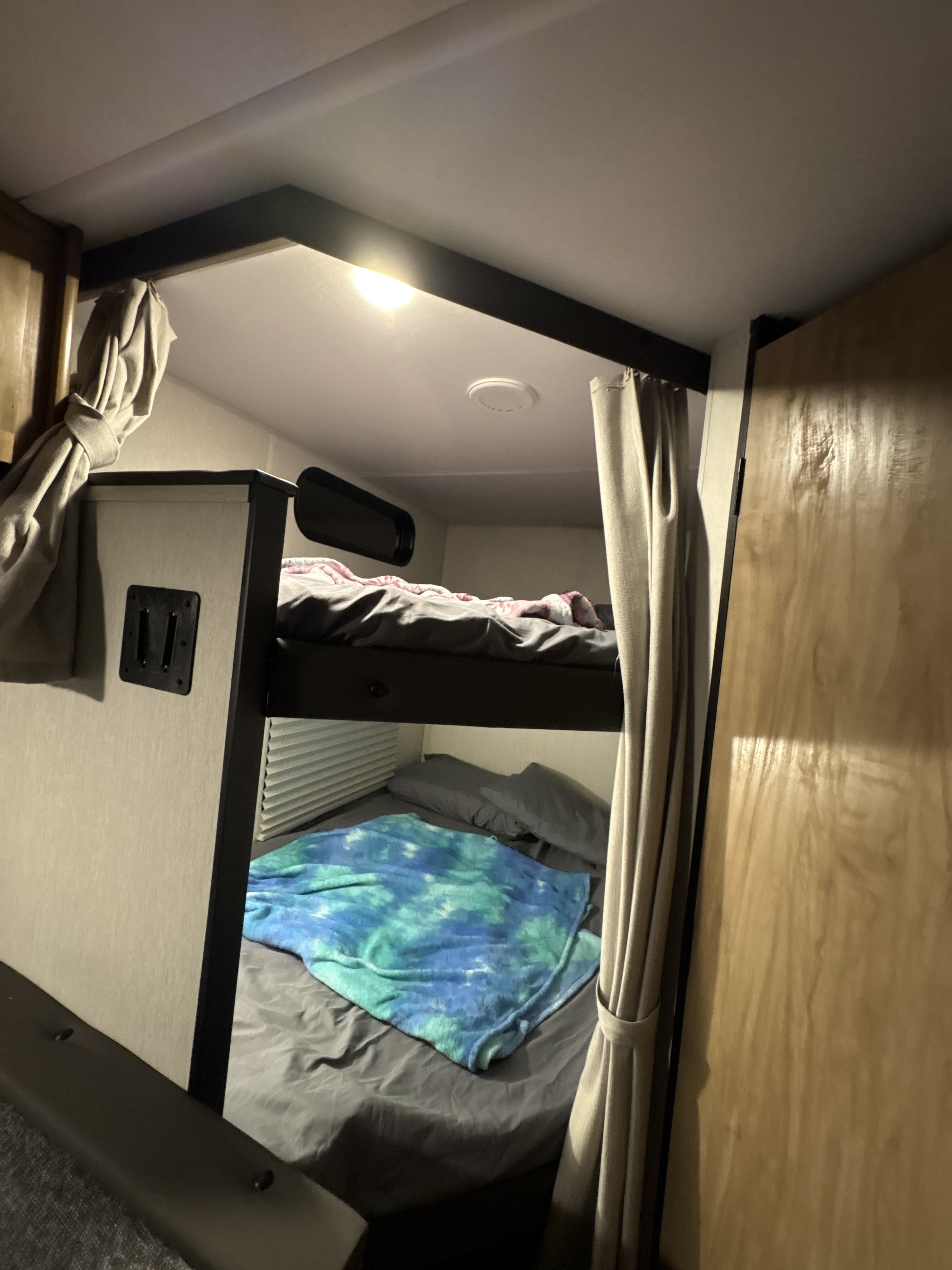 An RV rental's sleeping area, featuring cozy bunk beds with curtains and a tie-dye blanket on the lower bunk.. Forest River Cherokee Grey Wolf 2024