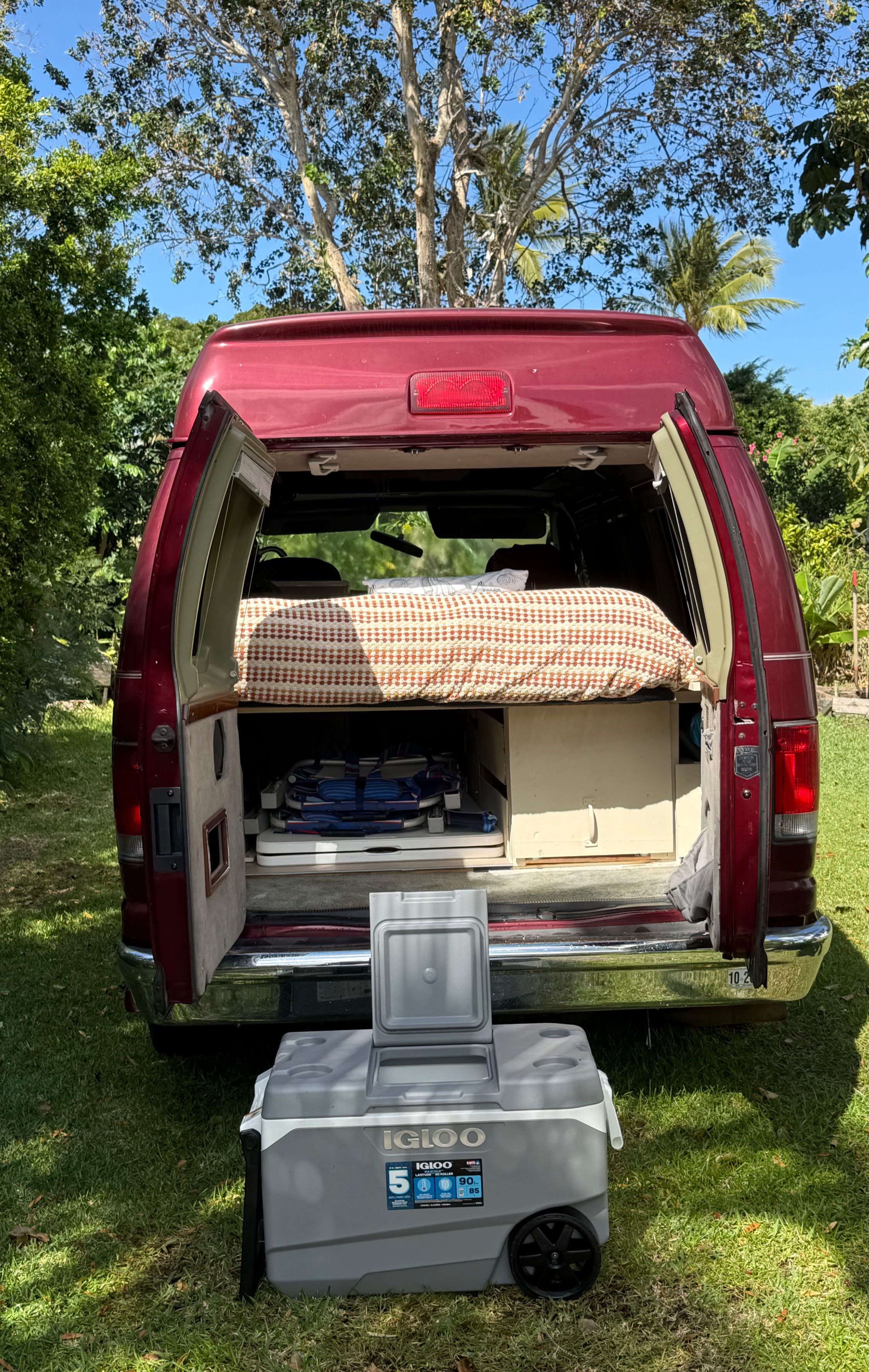 Red camper van with open rear doors, revealing a bed, camping gear, and an Igloo cooler. Ideal for your rv rental getaway.. Ford Econoline Club Wagon 2005