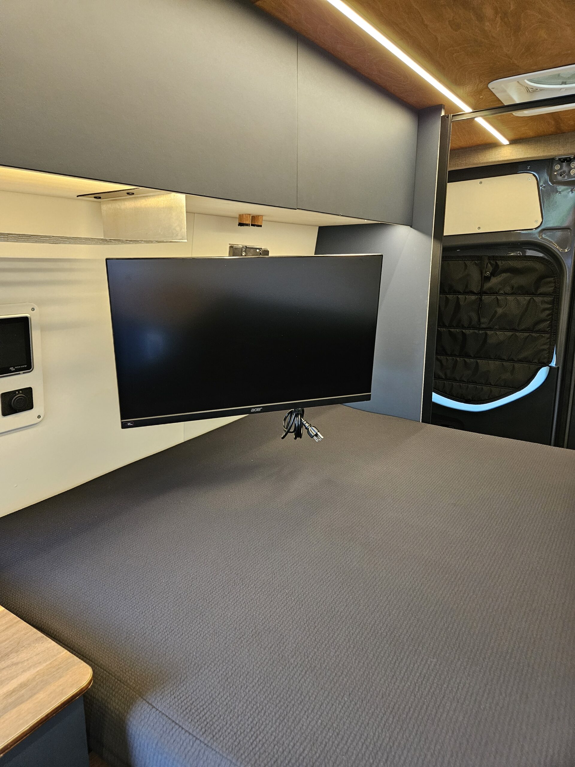 Modern campervan interior for your rv rental, showing a bed, mounted monitor, and overhead cabinets with lighting.. Venturhaus Sprinter 2022