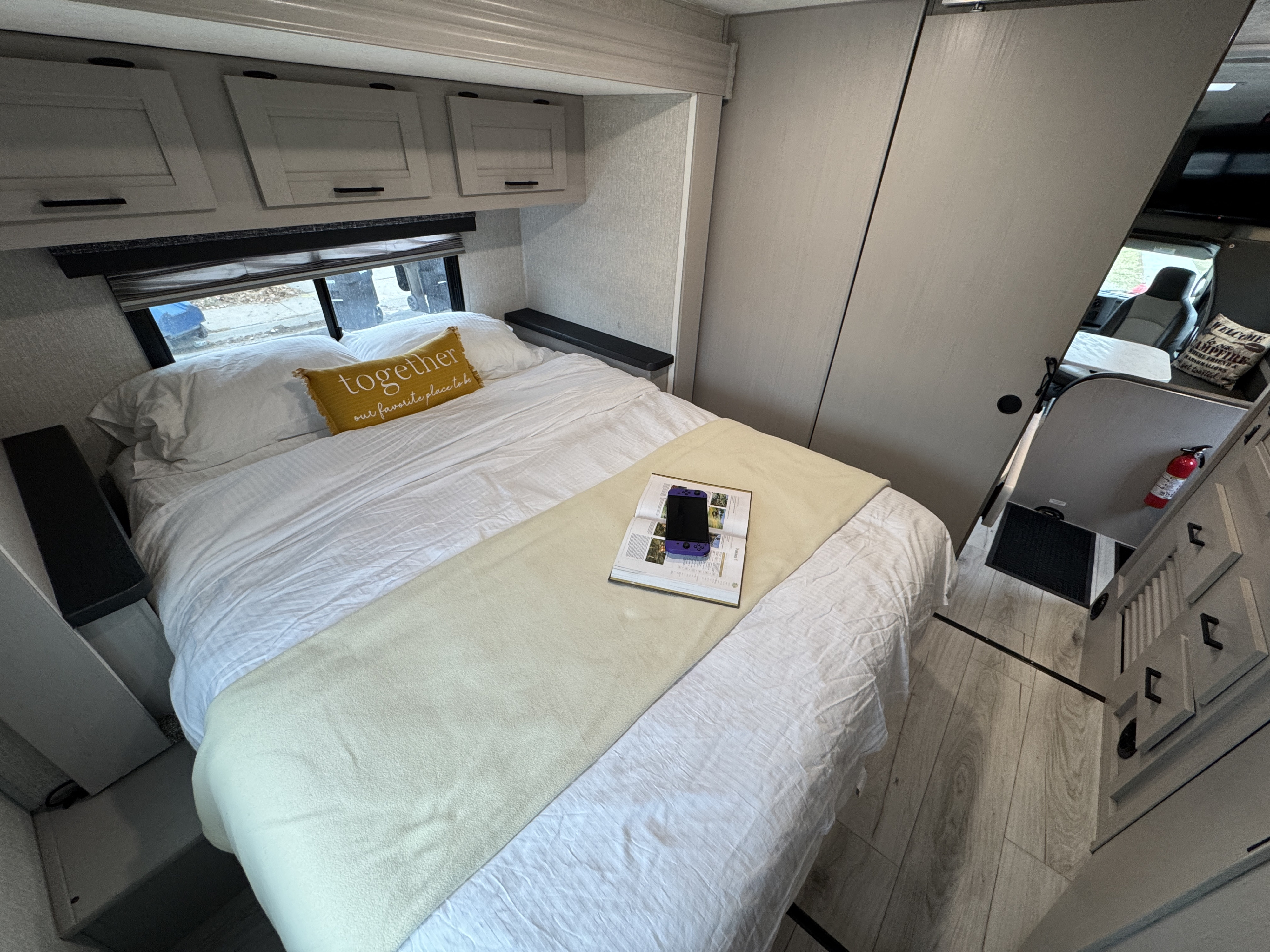 Cozy RV rental bedroom with a comfortable bed, yellow pillow, overhead cabinets, and a glimpse of the living area.. Forest River Coachmen Freelander 2025