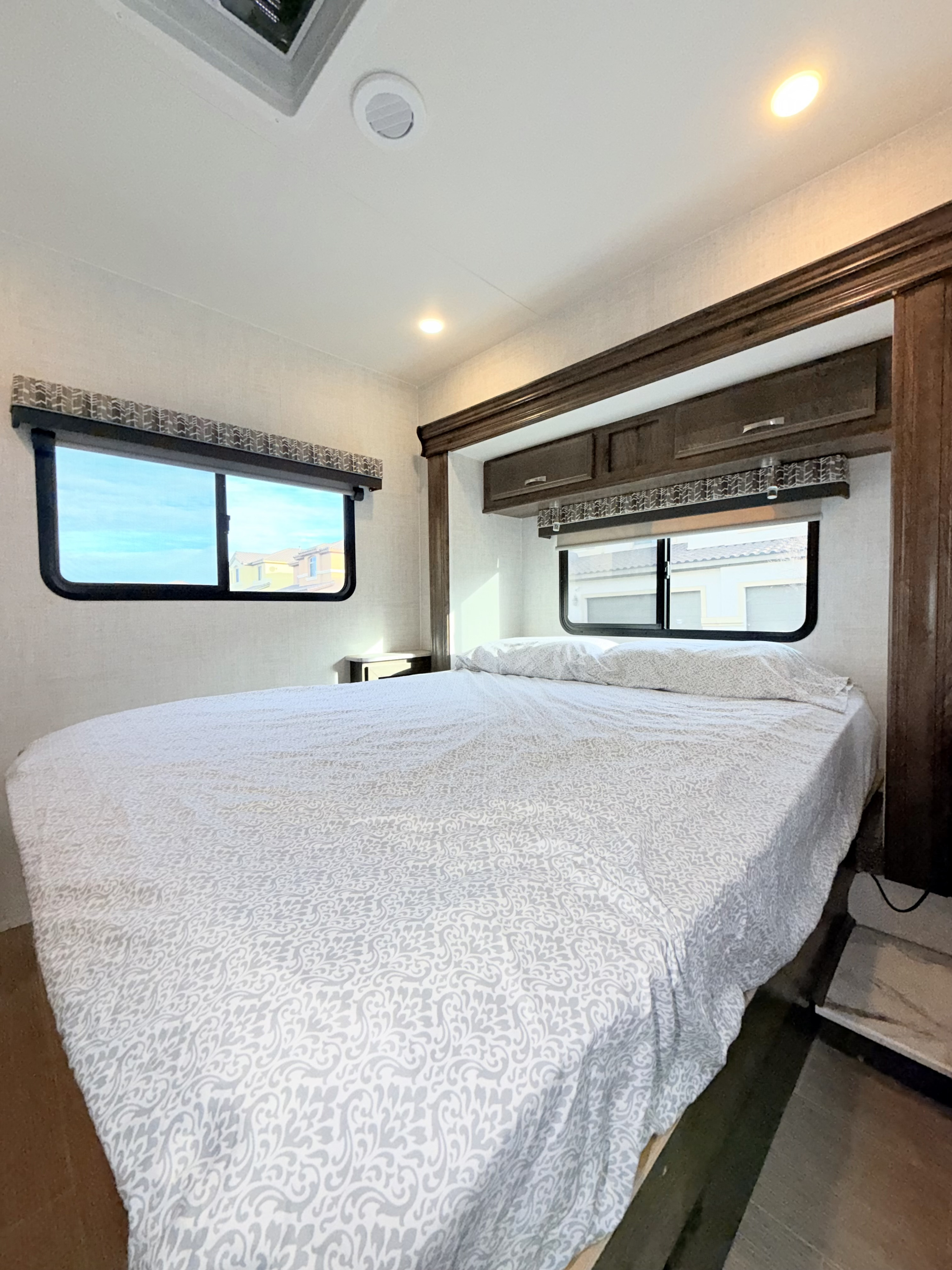 Cozy RV rental bedroom with a large bed, windows, and overhead storage. Ideal for comfortable travel accommodation.. Gulf Stream Conquest 2021