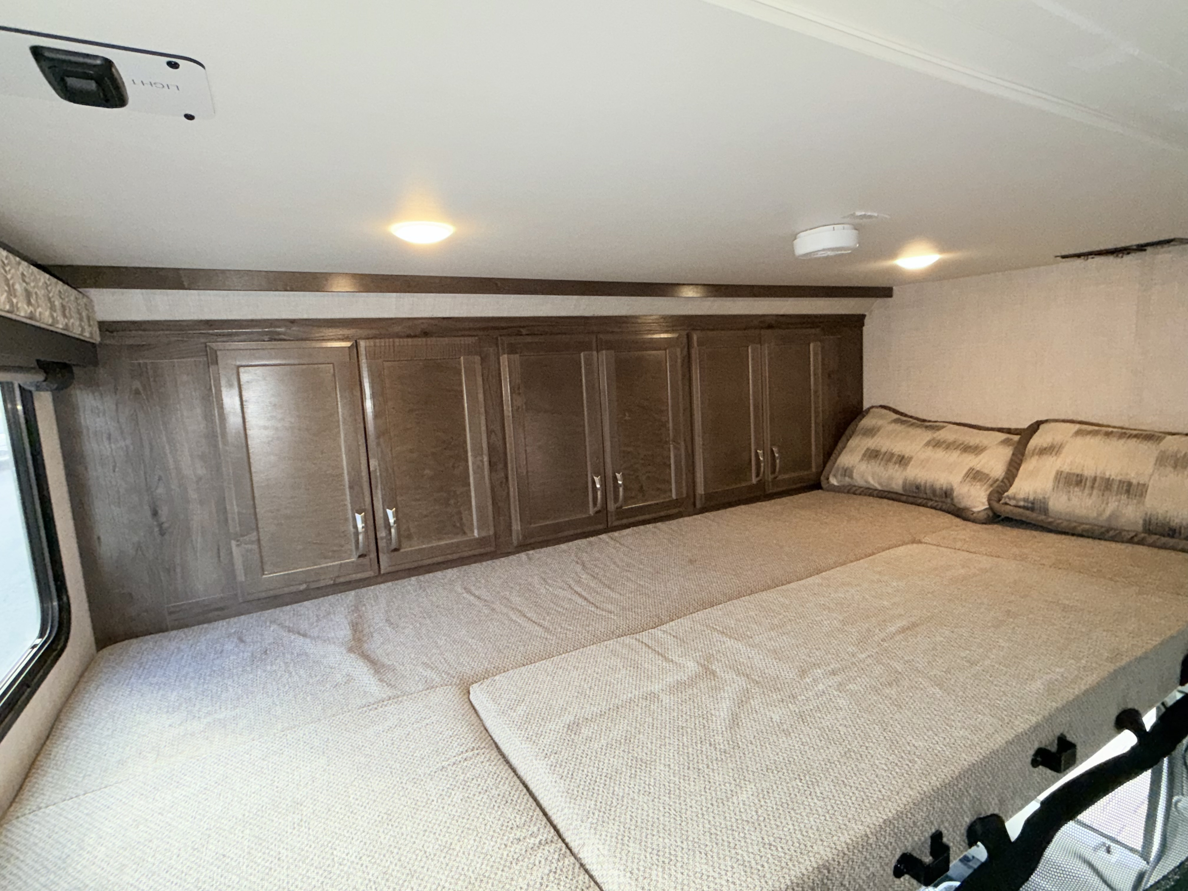 This RV rental features a cozy sleeping area with a large bed, wooden overhead cabinets, a window, and ceiling lights.. Gulf Stream Conquest 2021