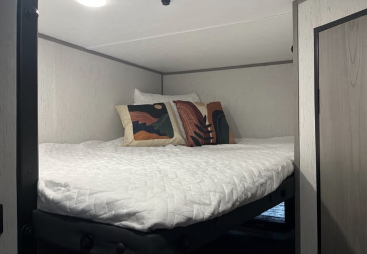 This RV rental bunk bed offers a cozy sleeping space with white bedding and stylish abstract pillows.. Dutchmen Coleman Lantern LT 2022