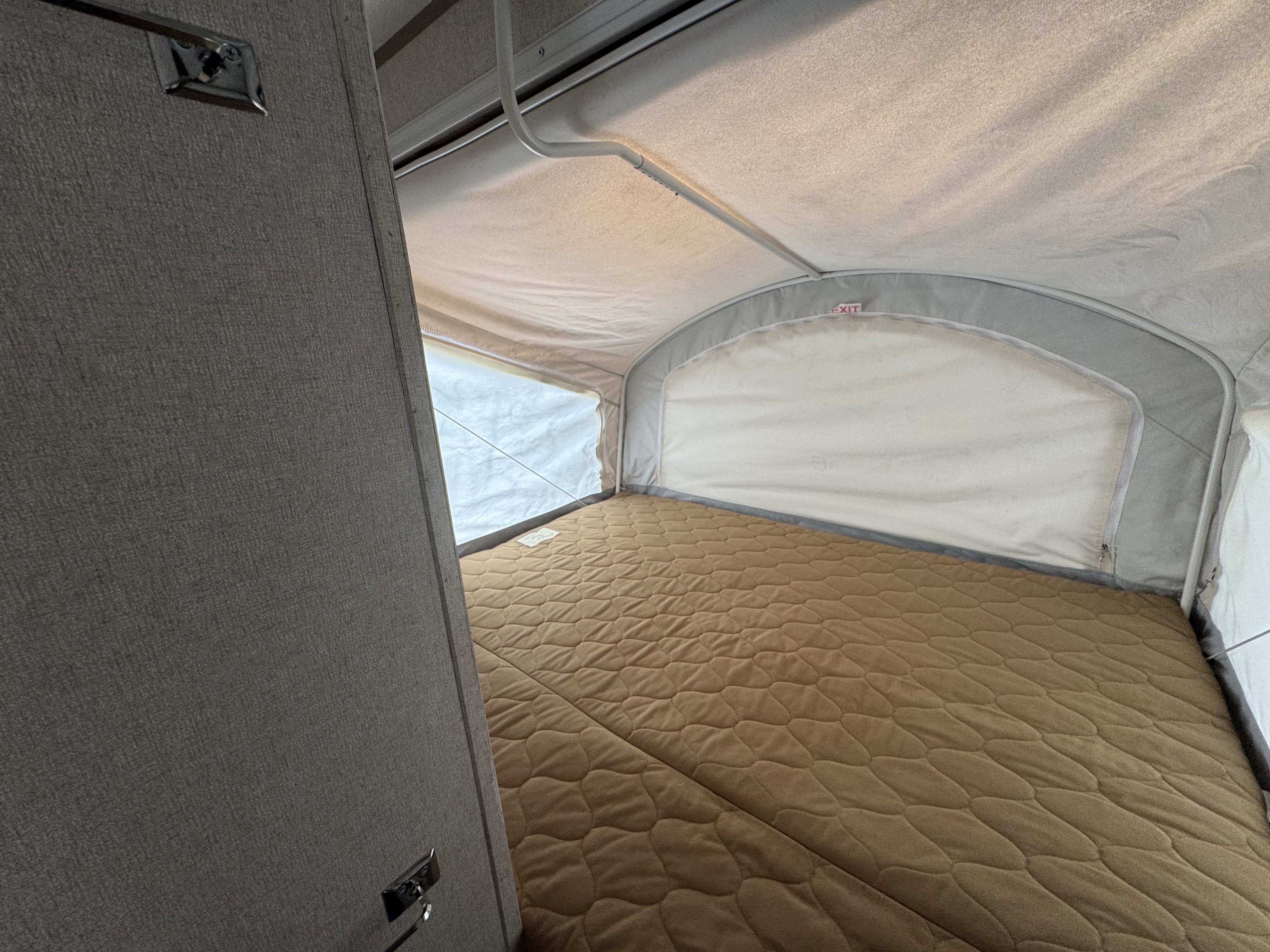 Inside an RV rental's pop-up camper: a comfy quilted bed, fabric walls, and an exit sign, ready for a restful night.. Coachmen Clipper 2019