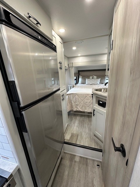 Modern RV rental interior: view of the hallway leading to the bedroom, past a stainless steel refrigerator & compact sink.. DynaMax iSata3 2025