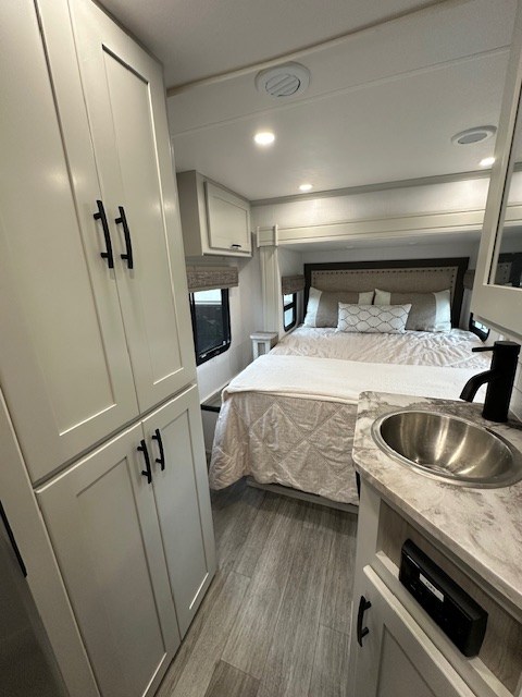 This rv rental's bedroom includes a cozy bed, ample storage cabinets, a compact sink, and wood-look flooring.. DynaMax iSata3 2025