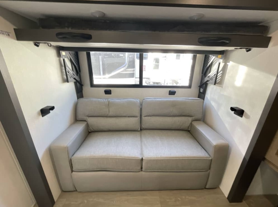 Compact RV rental interior featuring a comfortable light-grey sofa, window, and a fold-down bunk bed above.. FOREST RIVER Campsite Elite 36RF 2026