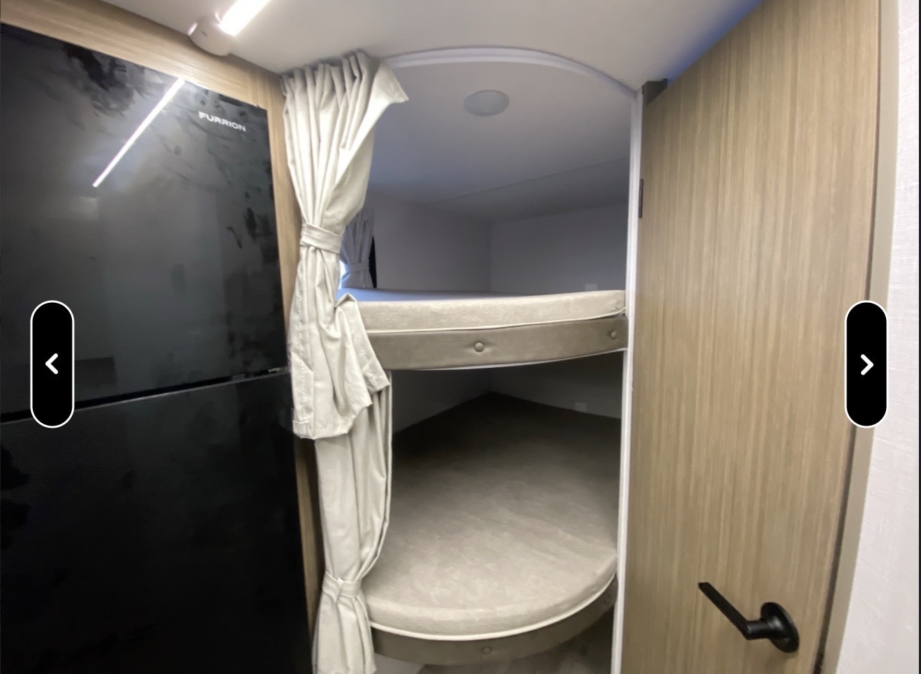 RV rental interior: Furrion refrigerator, two comfortable bunk beds with mattresses, curtains, and a wood door.. Forest River Wildwood BHSK 2026