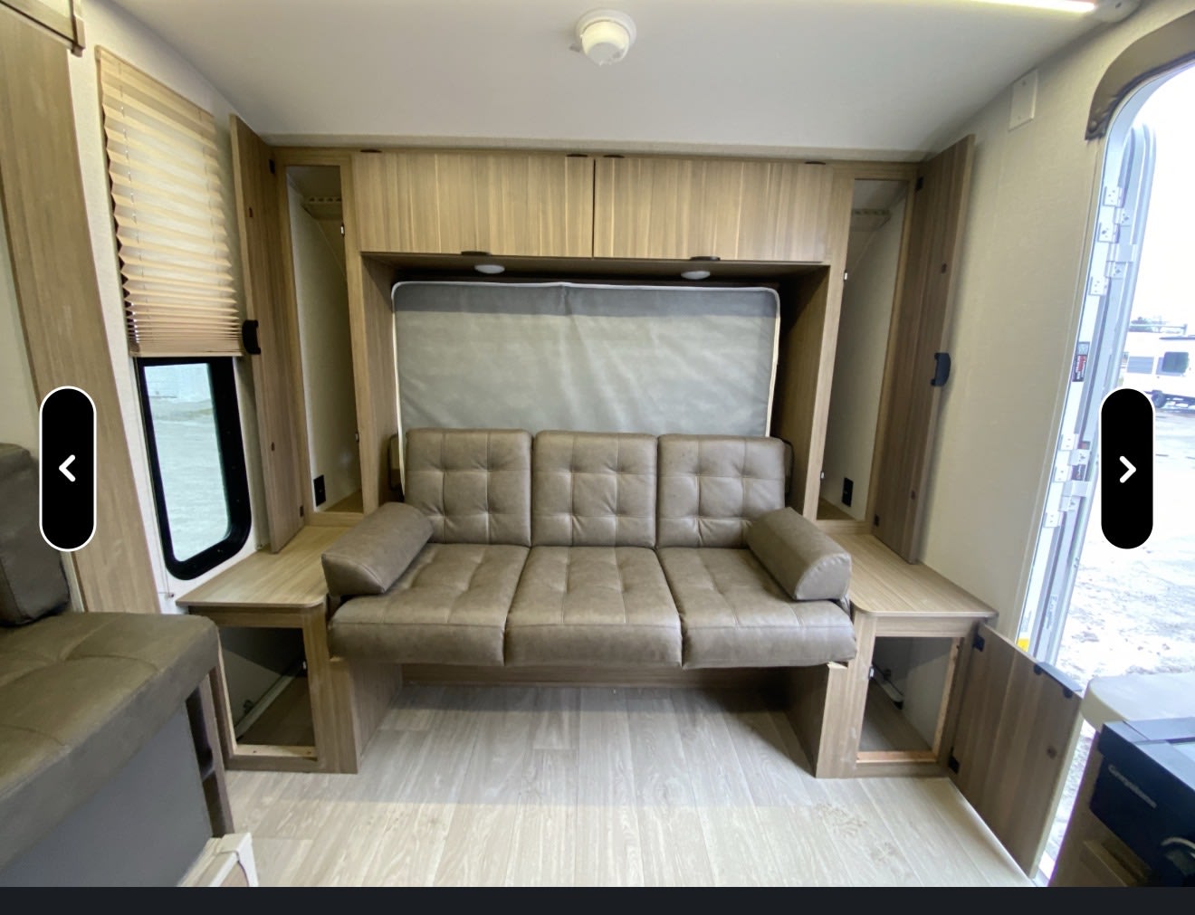 RV rental interior. Tufted sofa with a fold-up bed above, surrounded by wooden cabinets. Versatile living area.. Forest River Wildwood BHSK 2026