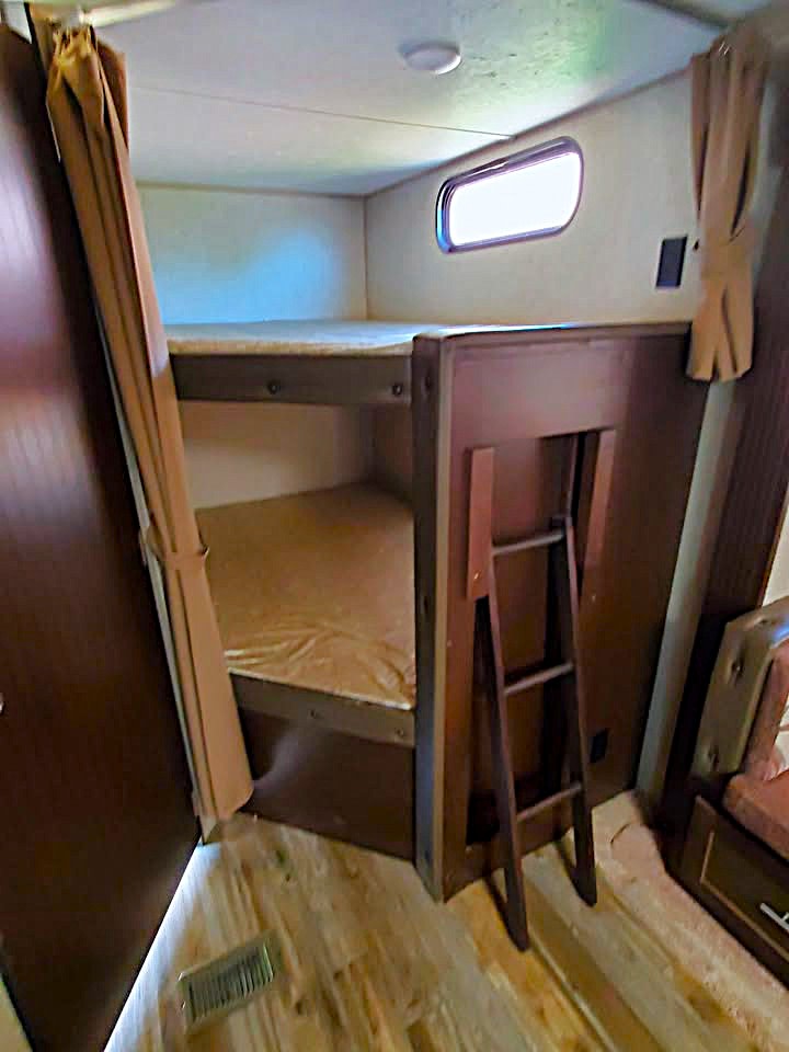 Cozy RV rental bunk beds with a ladder, window, and curtains, offering comfortable sleeping arrangements for travelers.. Forest River Cherokee 2016
