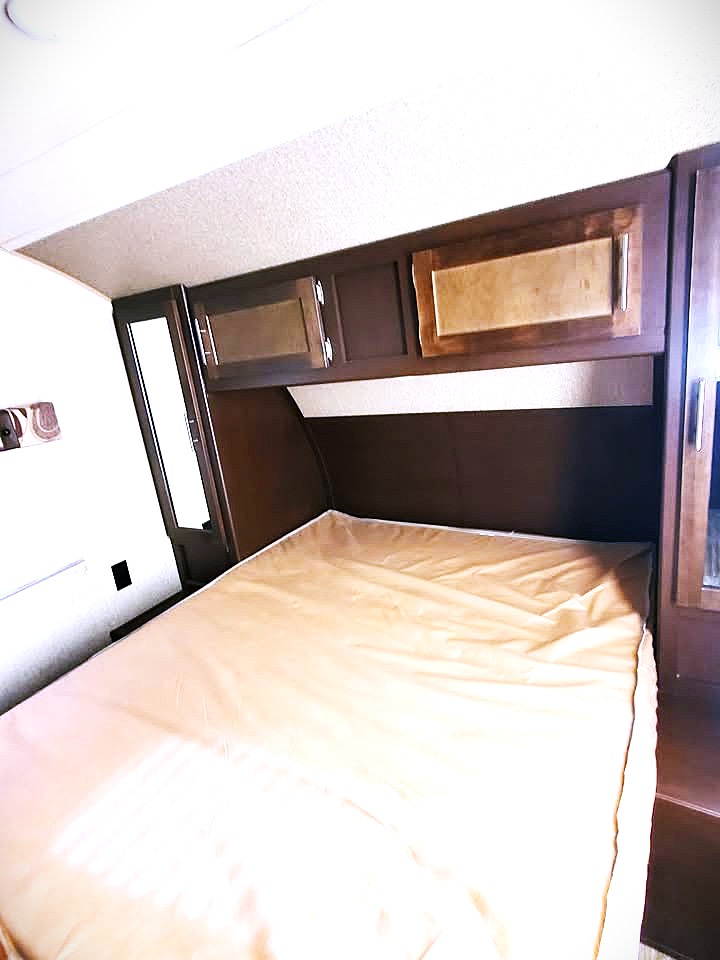 Interior of an RV rental bedroom showing a bed, headboard, and wood-toned overhead storage cabinets.. Forest River Cherokee 2016