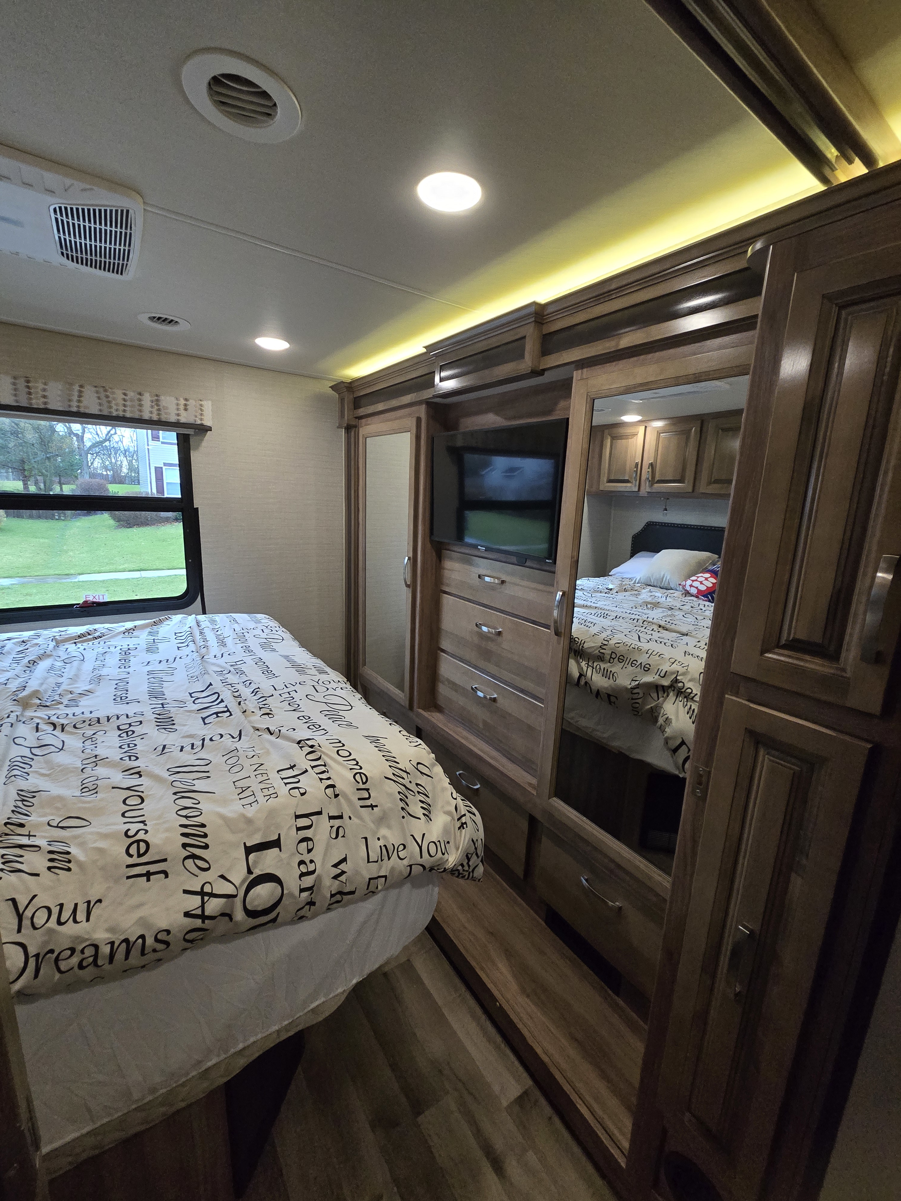 Cozy RV rental bedroom: bed, window, TV, and mirrored wardrobe reflect a comfortable interior.. Jayco Precept 2019