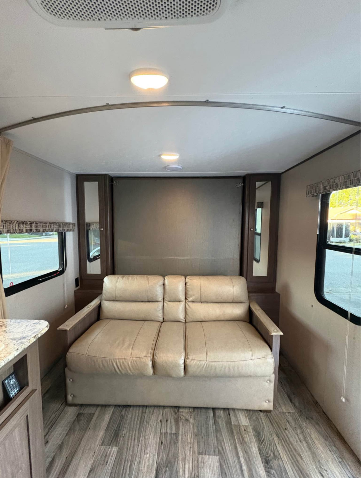 RV rental interior: A compact living space with a comfy tan sofa, side cabinet, large windows, and wood-look floor.. Keystone RV Hideout 2019
