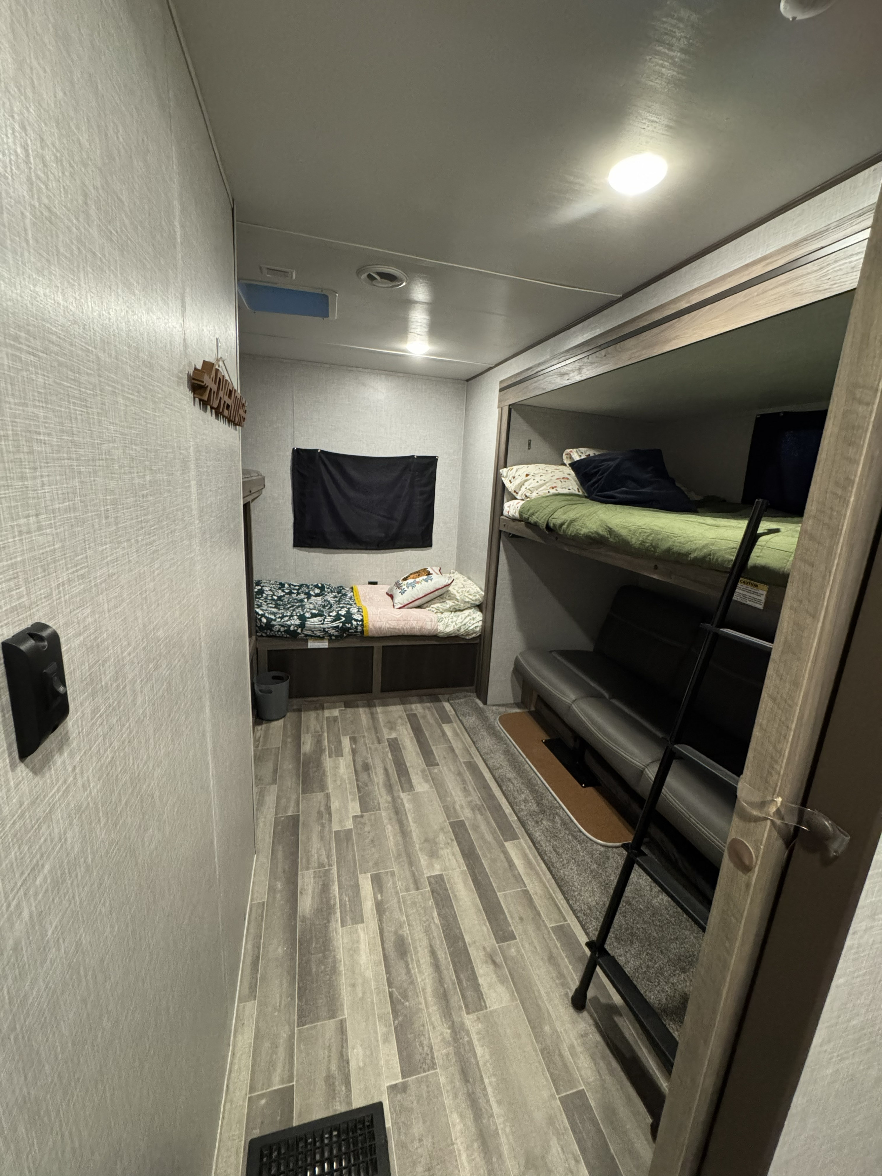 Cozy RV rental bunkhouse interior with multiple beds, a sofa, wood-look flooring, and ceiling lights, ideal for travel.. Crossroads RV Zinger 2022