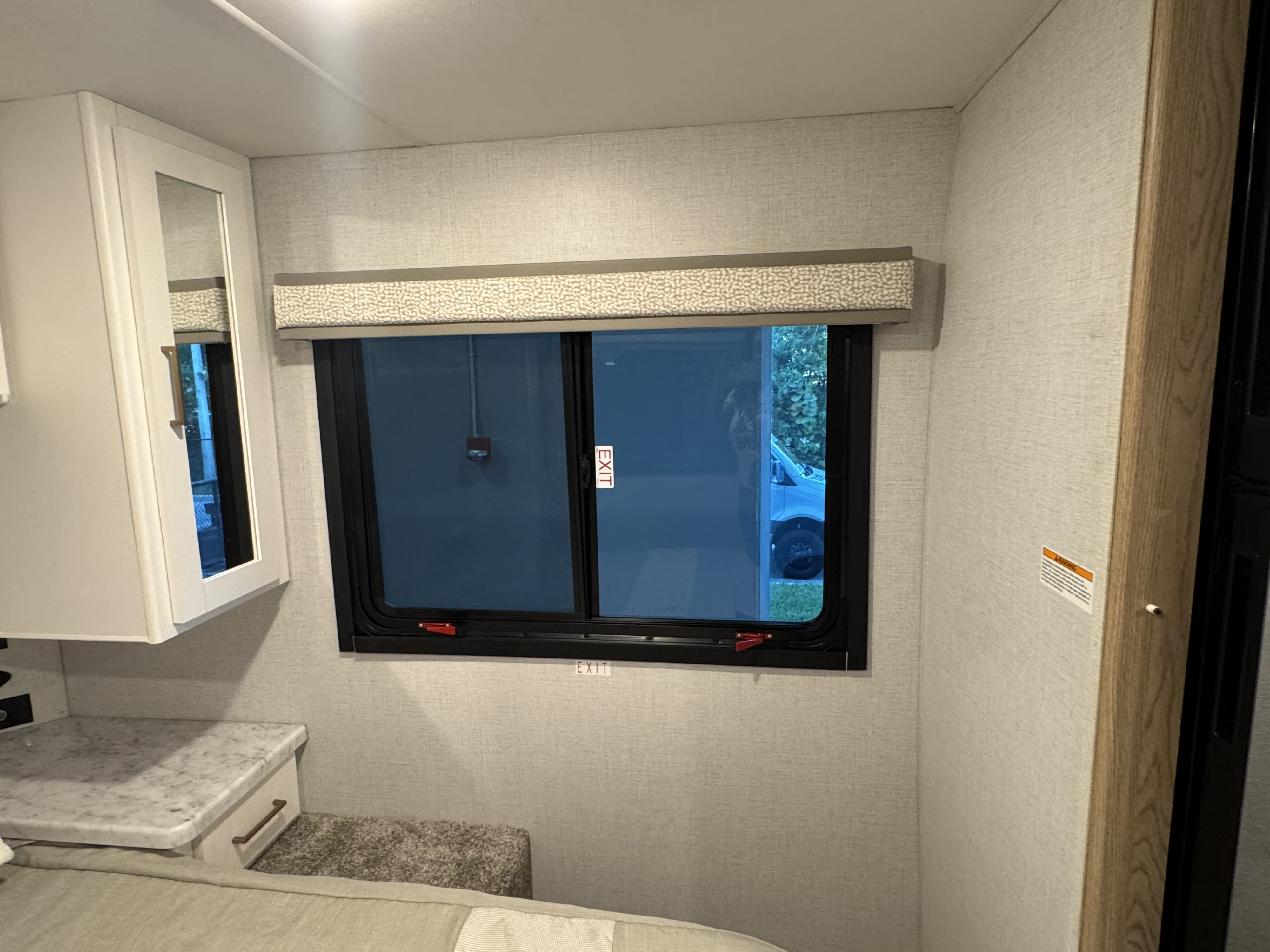 RV rental interior featuring a window with 'EXIT' label, patterned valance, mirrored cabinet, and nightstand by the bed.. 1FDXE4FN7TDD10505 Thor Chateau 2026