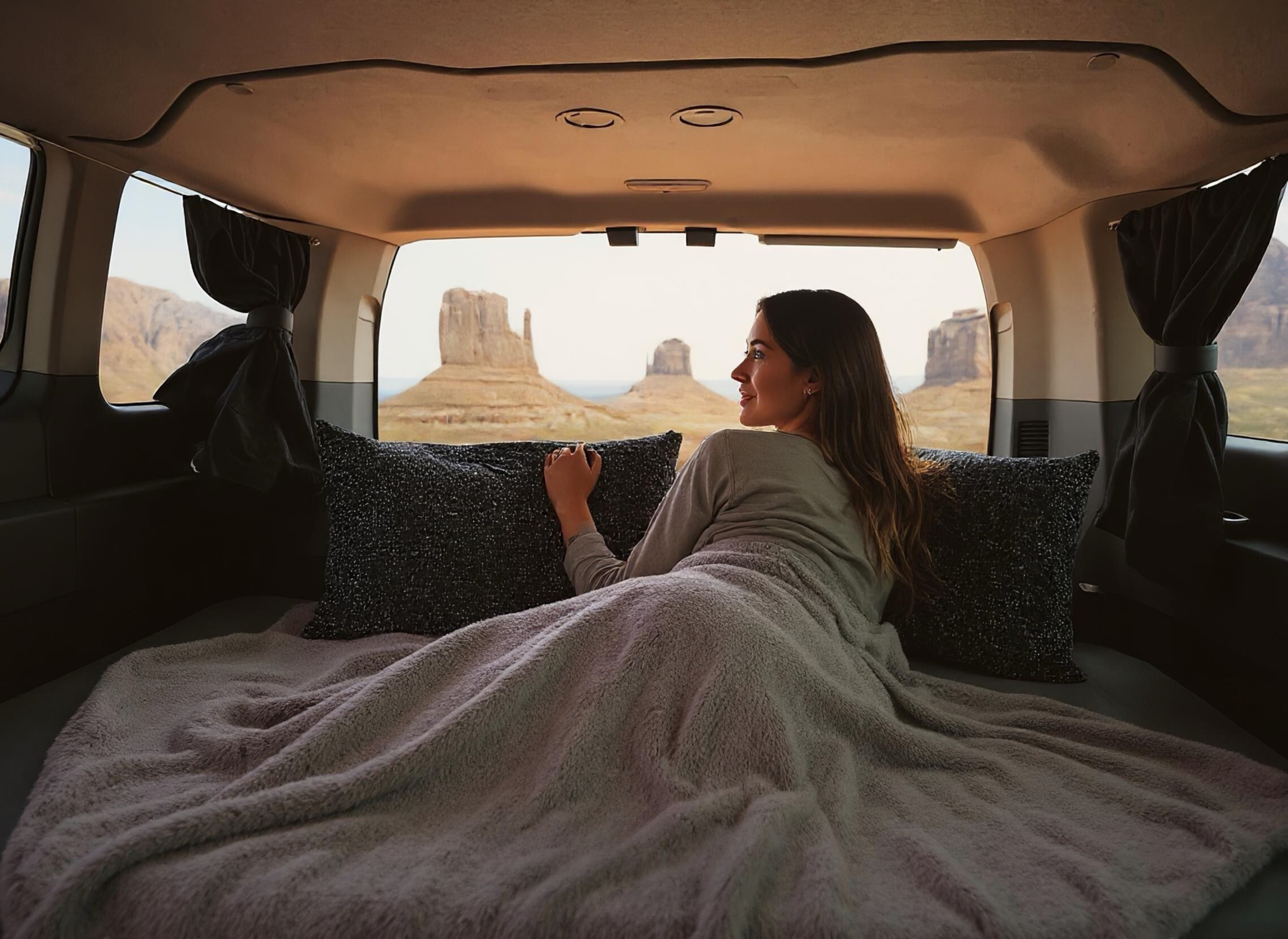 Cozy rv rental setup: A woman relaxes in bed, admiring Monument Valley's desert formations. Perfect for van life adventures!. Ford Transit 2017