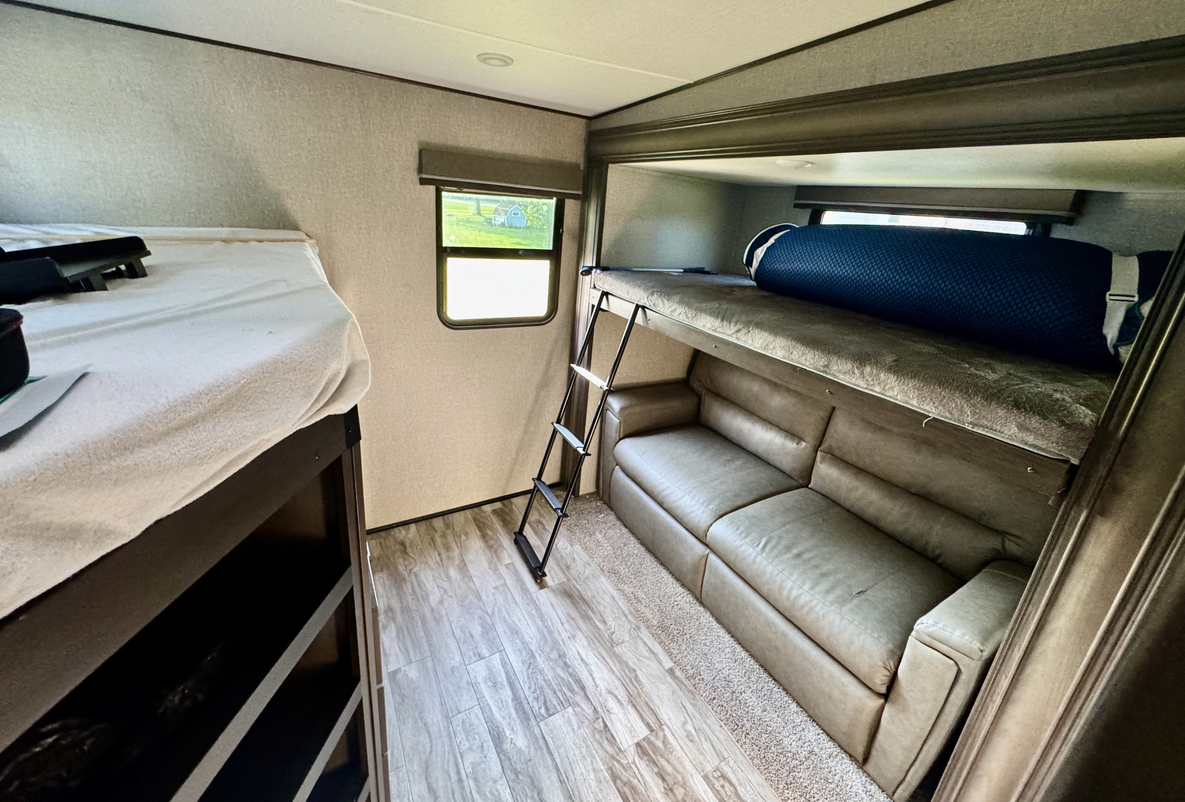 This rv rental bunk area features a ladder, sofa, and wood-look flooring, showcasing a compact and functional space.. Grand Design Reflection 2021