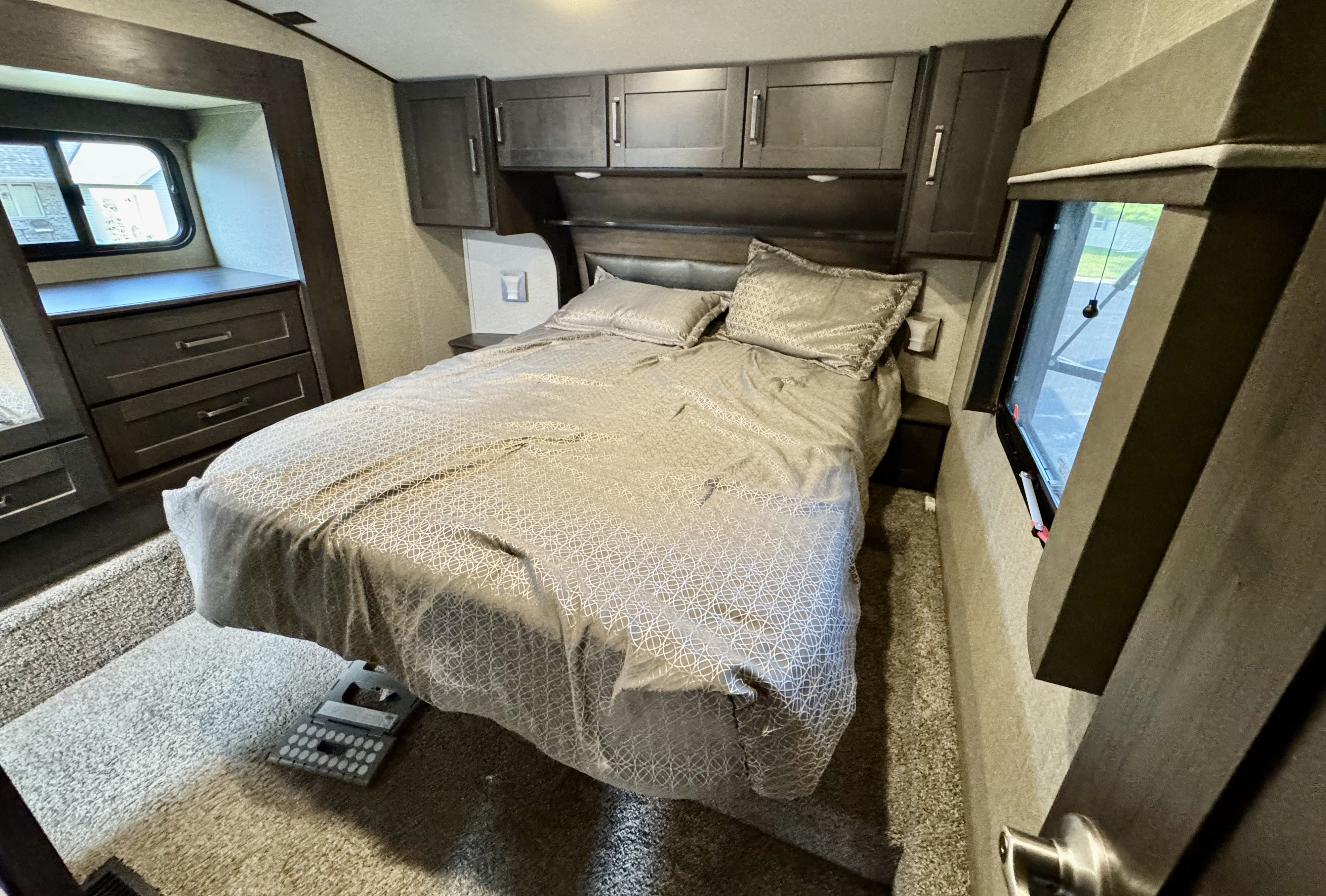 RV rental bedroom: a cozy space with a bed, geometric sheets, dark cabinetry, and windows on both sides.. Grand Design Reflection 2021