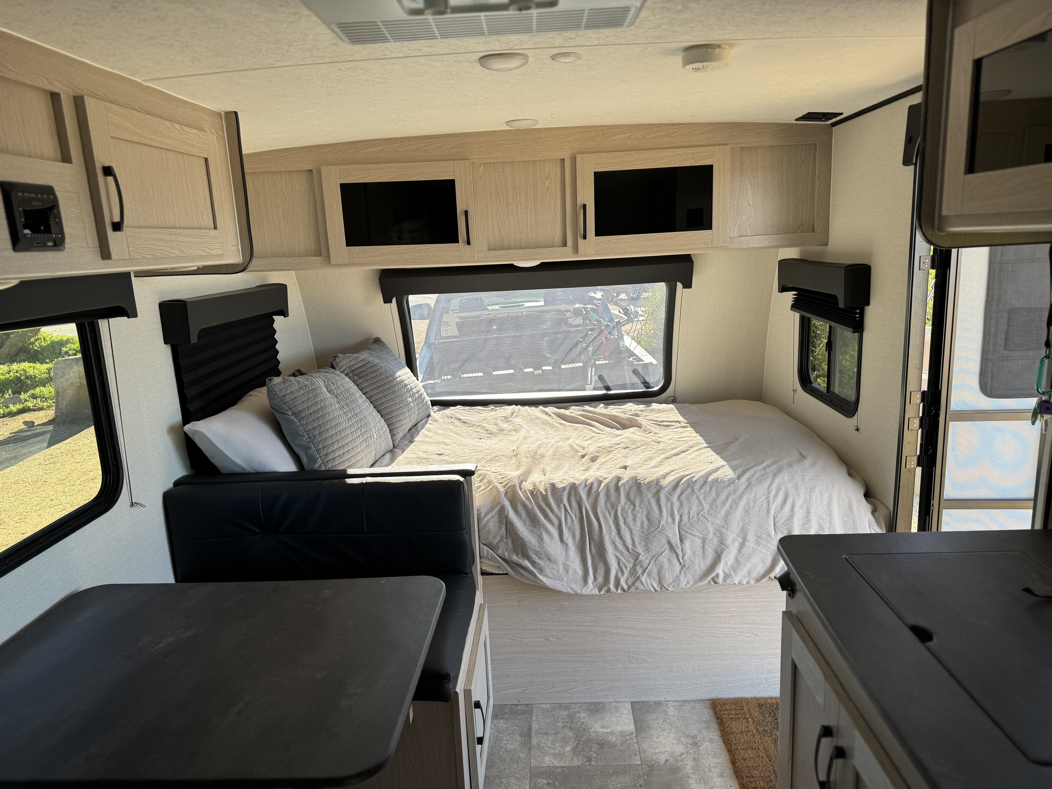 Modern rv rental interior: a comfy bed, black dinette, light wood cabinets, windows, and control panel. Bright and functional space.. Forest River APEX NANO 185BH 2022