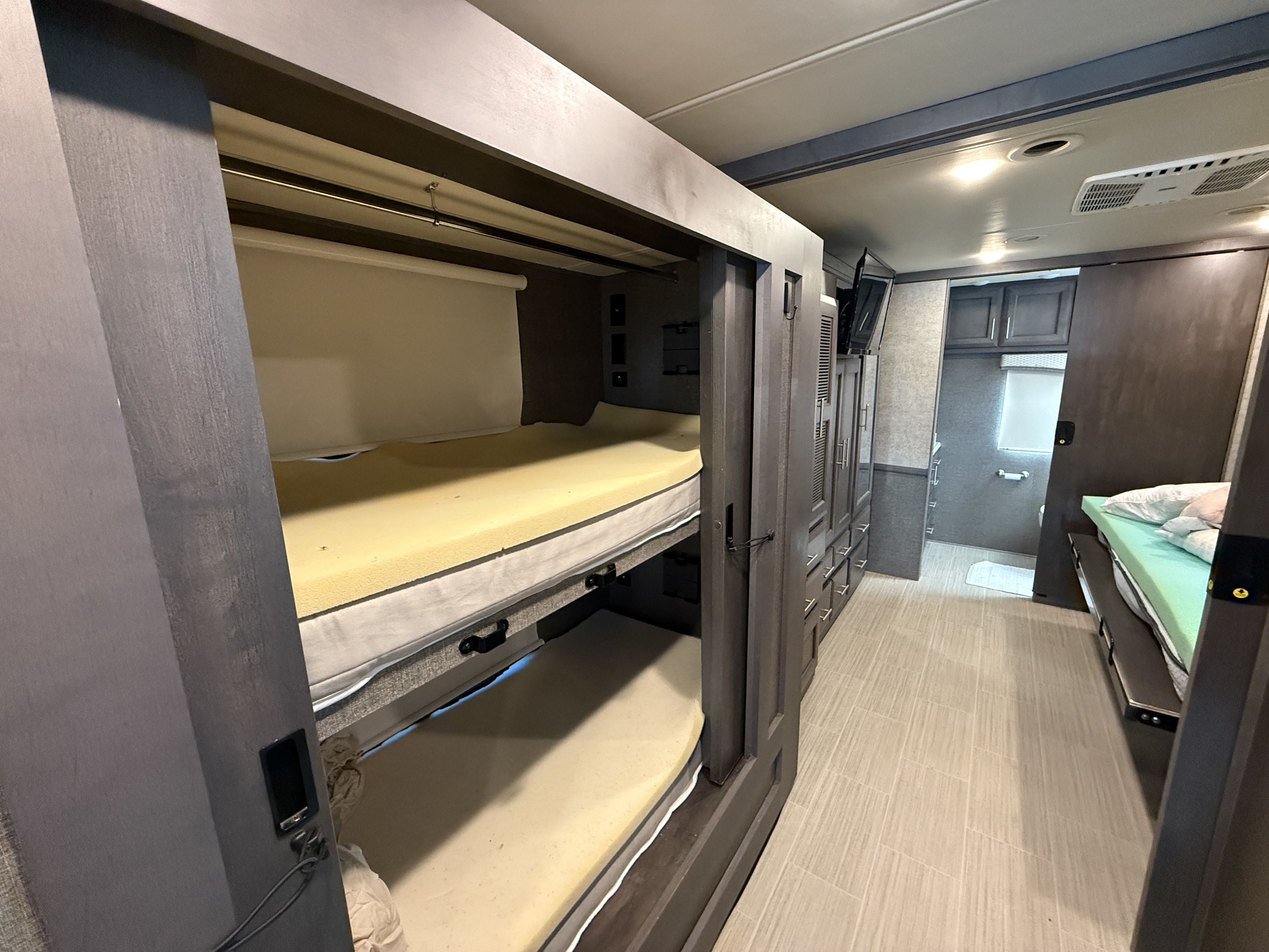 An RV rental's interior showcasing comfortable bunk beds, ample storage cabinets, and a convenient bathroom area.. Ford Thor Challenger 2021