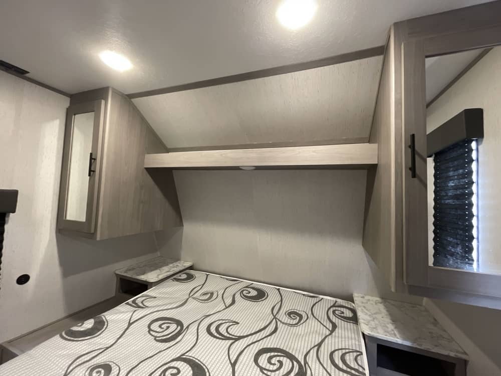 Cozy RV rental bedroom with a comfortable bed, mirrored overhead cabinets, and a window with a blind for your travels.. Keystone RV Coleman 2020