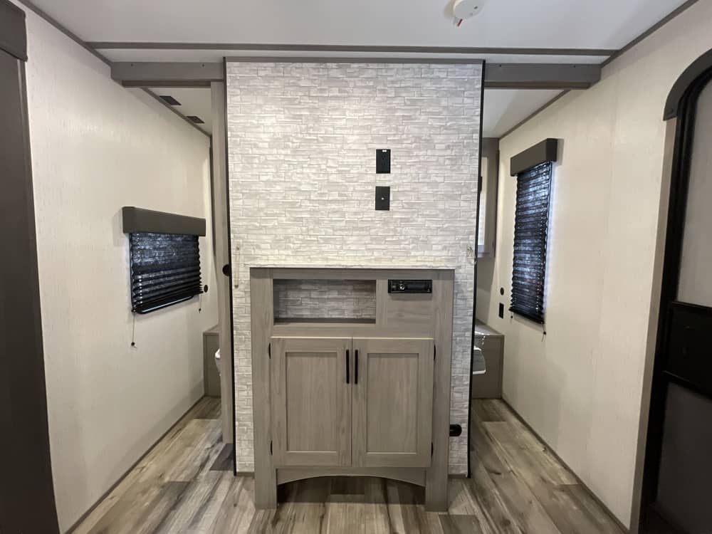 RV rental interior shows a central media unit dividing two hallways leading to private rooms with windows and wood-look floors.. Keystone RV Coleman 2020