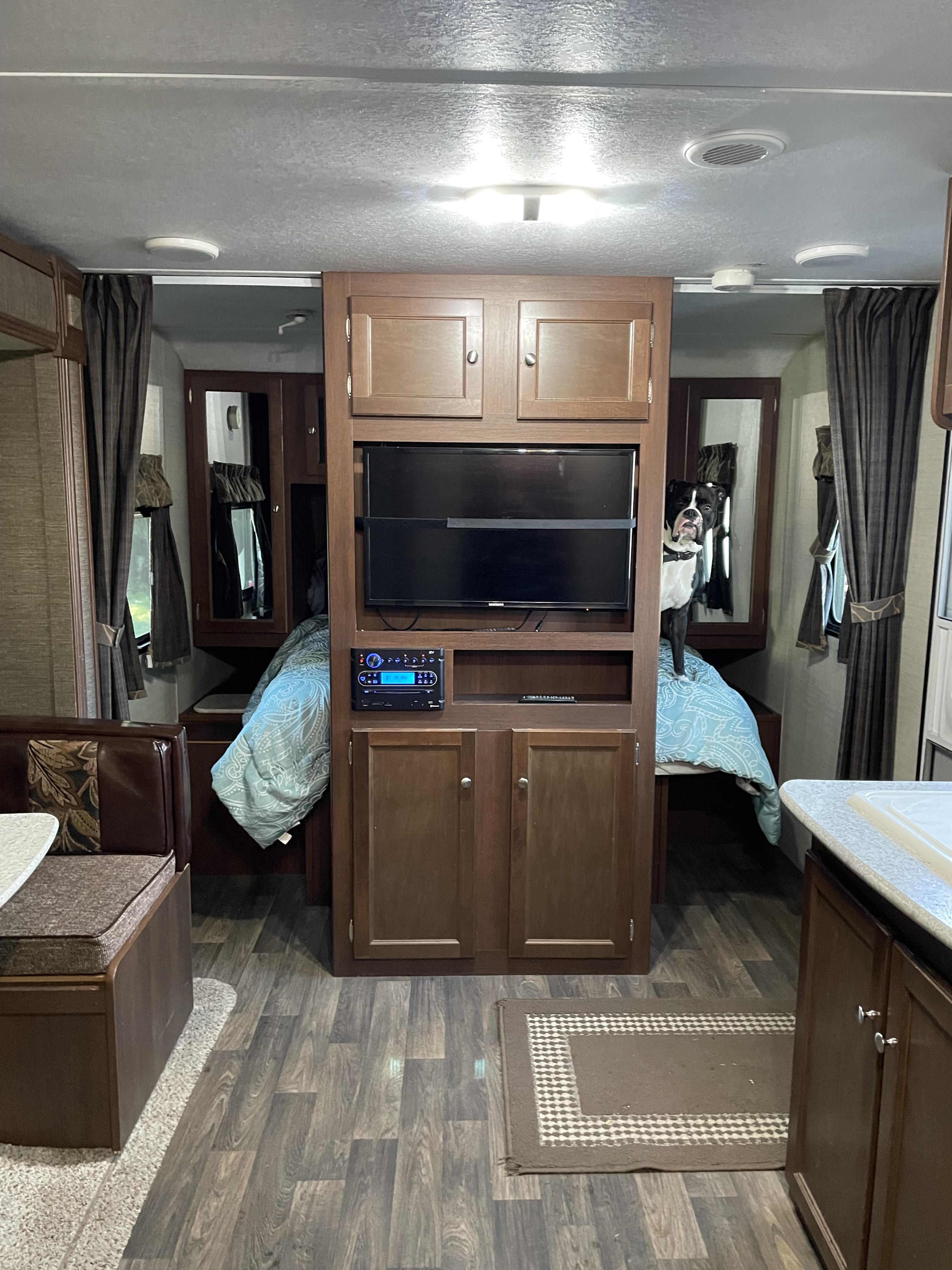 RV rental interior with a central entertainment unit, dinette, and a bedroom where a black and white dog stands on the bed.. Keystone RV Bullet Ultra Lite 2015