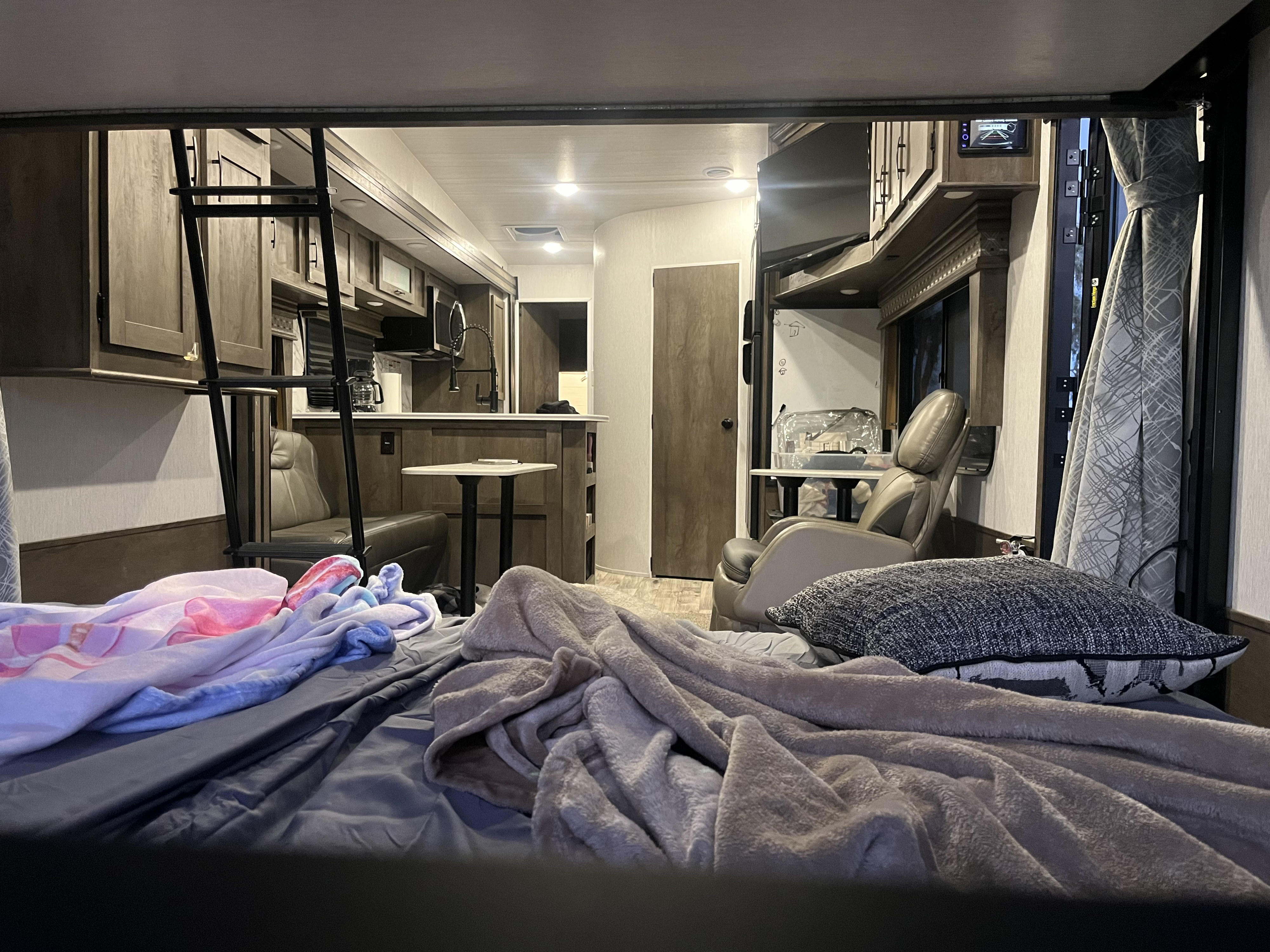 Inside an RV rental: foreground bed with blankets, ladder to a bunk, full kitchen, and comfy recliner.. Forest River Sandstorm 2022